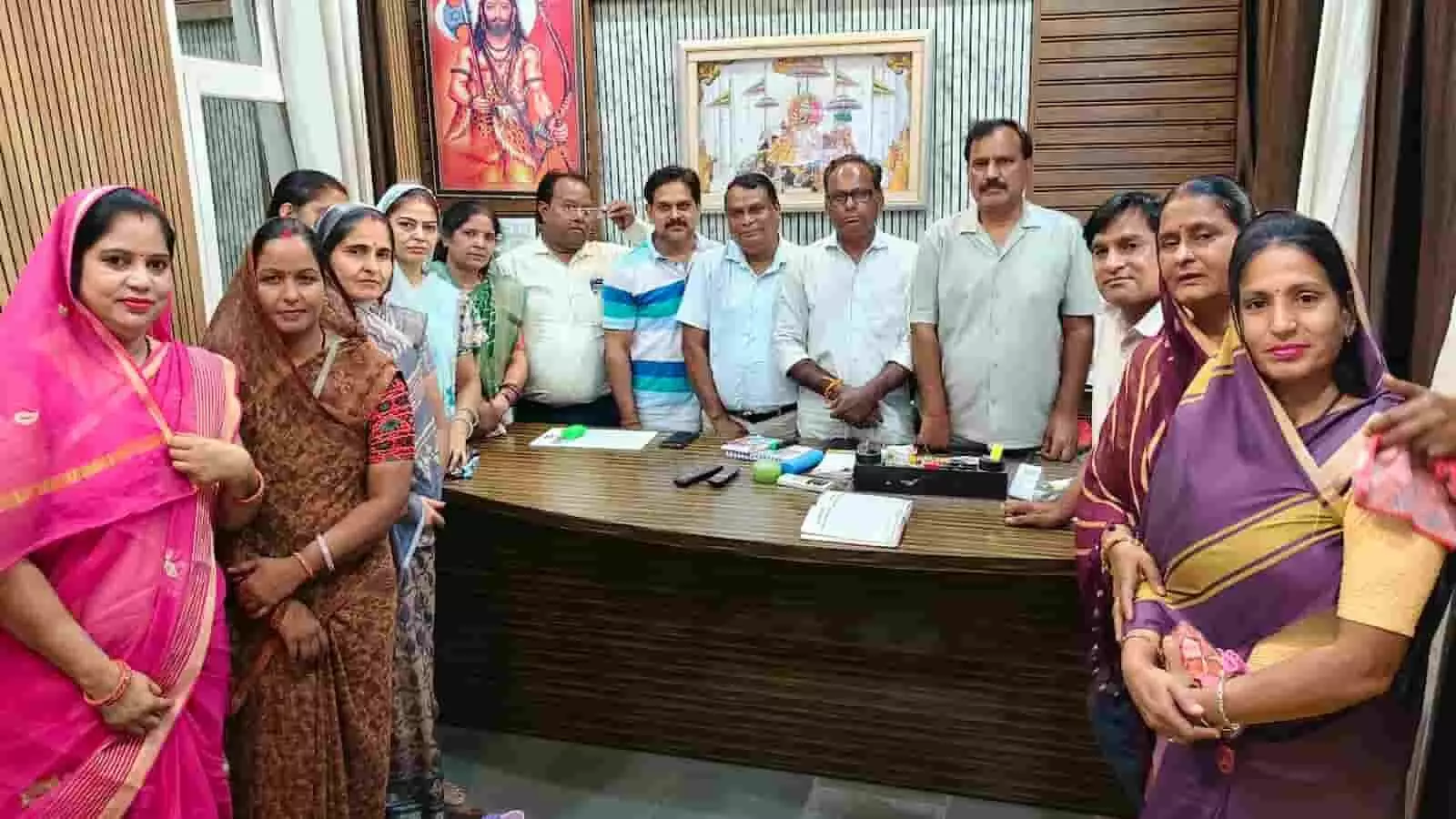 तस्वीर में सर्व ब्राह्मण महासभा के महिला और पुरुष सदस्य एक कार्यालय के कमरे में मेज के पास खड़े हैं। तस्वीर में सर्व ब्राह्मण महासभा के महिला और पुरुष सदस्य एक कार्यालय के कमरे में मेज के पास खड़े हैं।