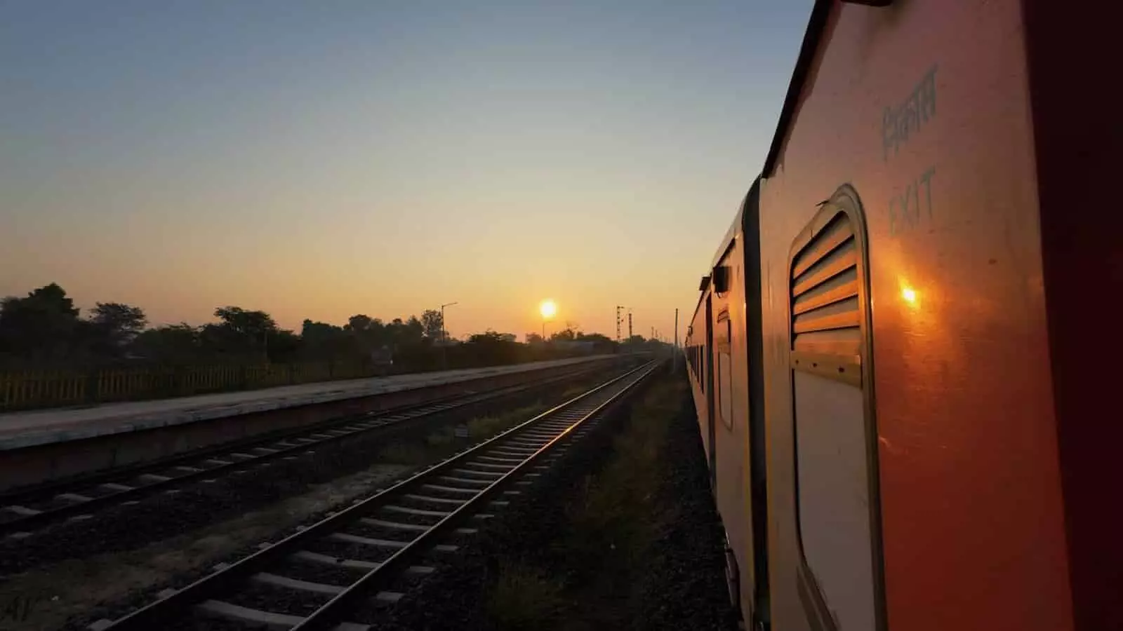 तस्वीर में सुबह के समय रेलवे ट्रैक पर खड़ी ट्रेन और सूर्योदय का दृश्य दिख रहा है। तस्वीर में सुबह के समय रेलवे ट्रैक पर खड़ी ट्रेन और सूर्योदय का दृश्य दिख रहा है।