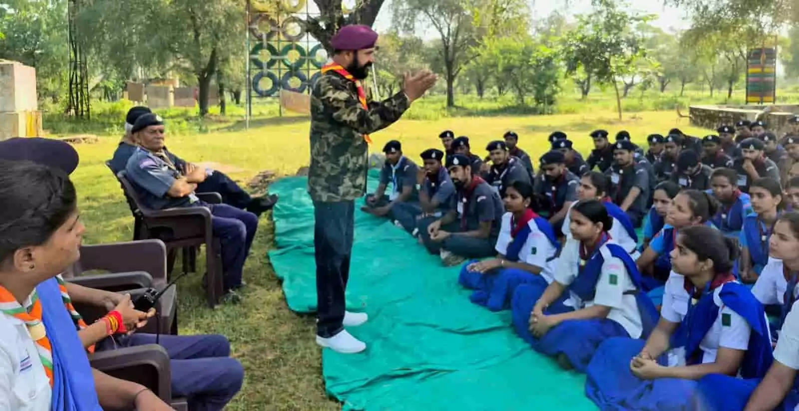 तस्वीर में स्काउट-गाइड की पोशाक पहने प्रतिभागी जमीन पर बैठकर अधिकारी का संबोधन सुन रहे हैं। तस्वीर में स्काउट-गाइड की पोशाक पहने प्रतिभागी जमीन पर बैठकर अधिकारी का संबोधन सुन रहे हैं।