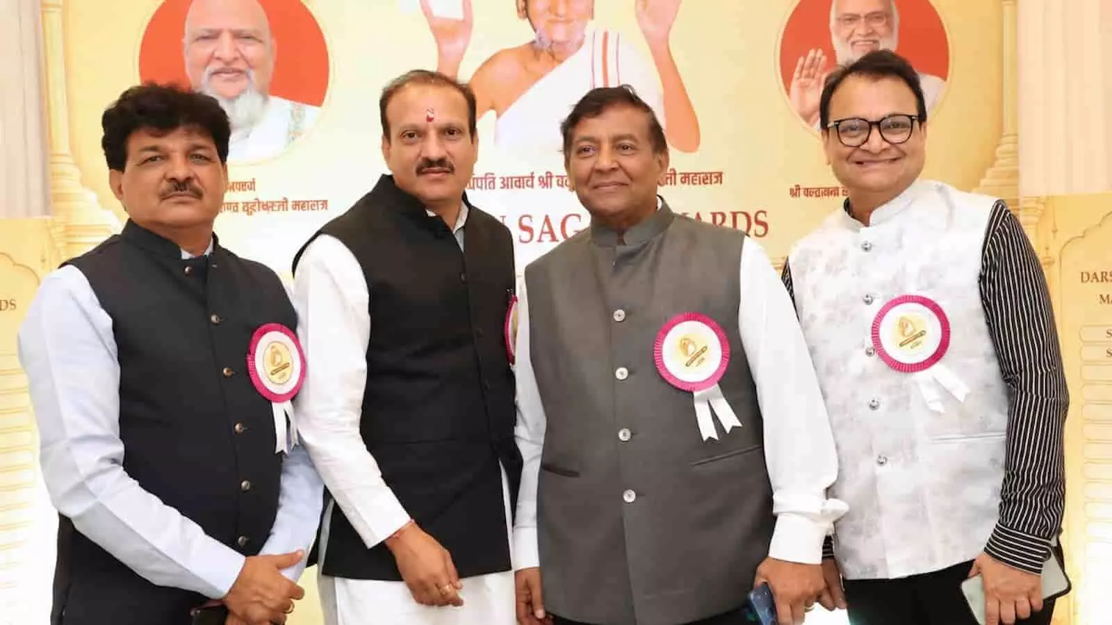 तस्वीर में चार सम्मानित व्यक्ति मंच पर खड़े हैं और पृष्ठभूमि में संतों के चित्र दिख रहे हैं। तस्वीर में चार सम्मानित व्यक्ति मंच पर खड़े हैं और पृष्ठभूमि में संतों के चित्र दिख रहे हैं।