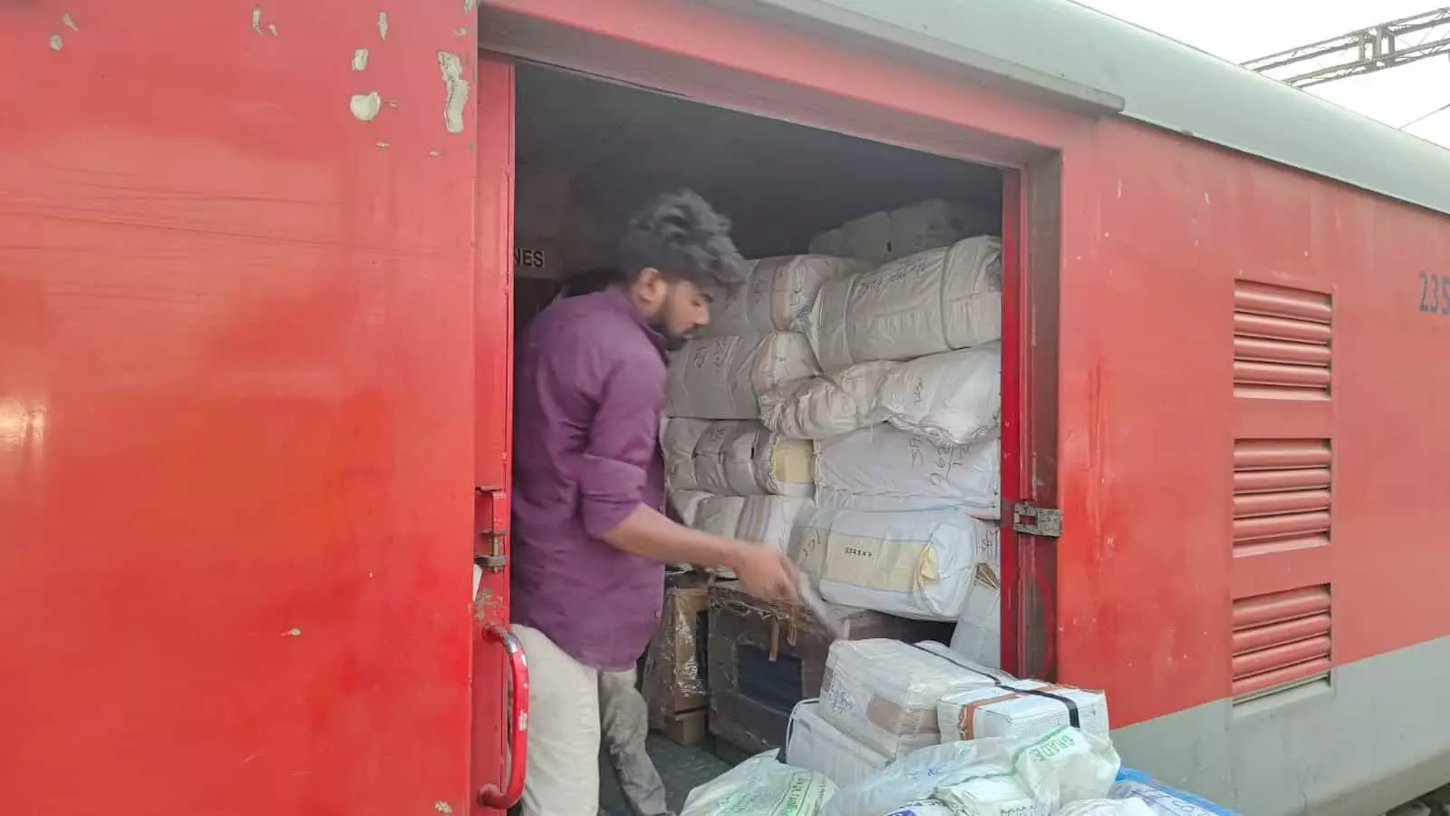 लाल रंग के ट्रेन कोच के खुले पार्सल डिब्बे में सामान लोड करता हुआ एक रेल कर्मचारी। लाल रंग के ट्रेन कोच के खुले पार्सल डिब्बे में सामान लोड करता हुआ एक रेल कर्मचारी।