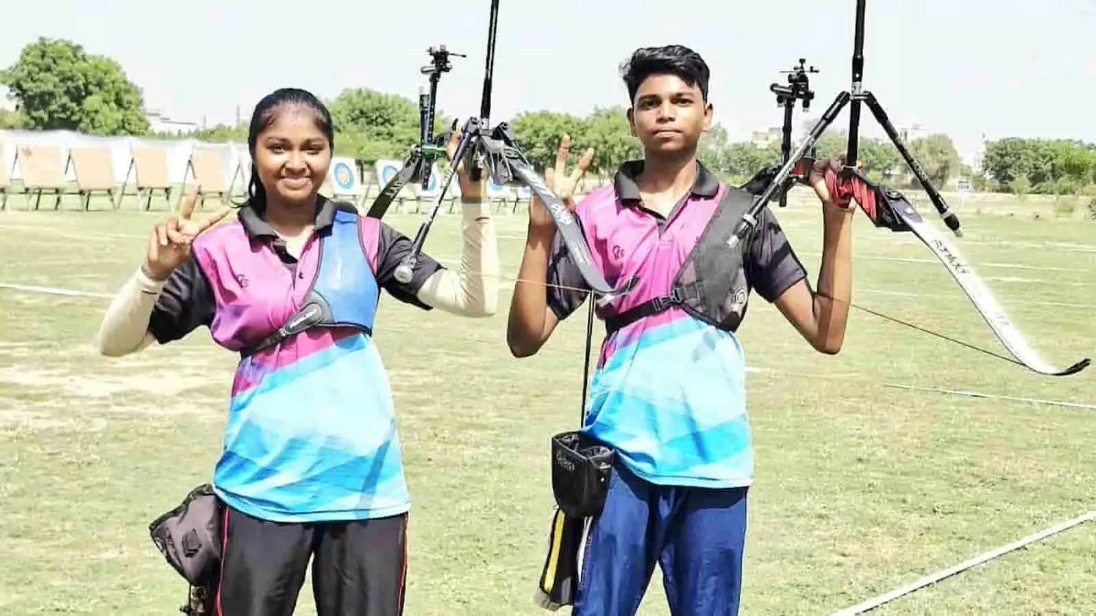 तस्वीर में बाएं से दाएं दो युवा तीरंदाज मैदान में धनुष थामे विक्ट्री साइन बना रहे हैं। तस्वीर में बाएं से दाएं दो युवा तीरंदाज मैदान में धनुष थामे विक्ट्री साइन बना रहे हैं।
