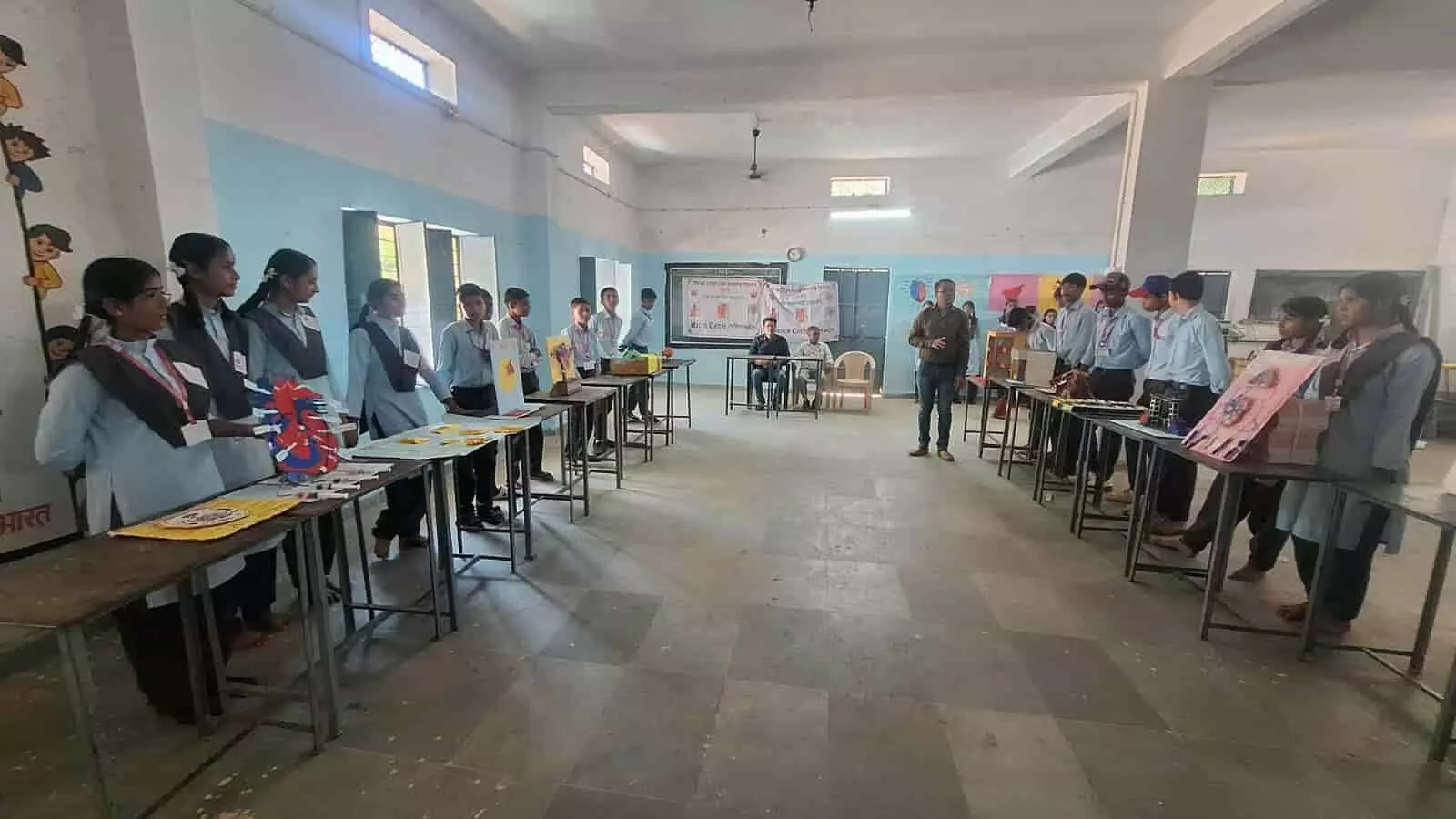 तस्वीर में दिख रही कक्षा में छात्र-छात्राएं मेजों पर रखे विज्ञान मॉडलों के पास खड़े हैं। तस्वीर में दिख रही कक्षा में छात्र-छात्राएं मेजों पर रखे विज्ञान मॉडलों के पास खड़े हैं।