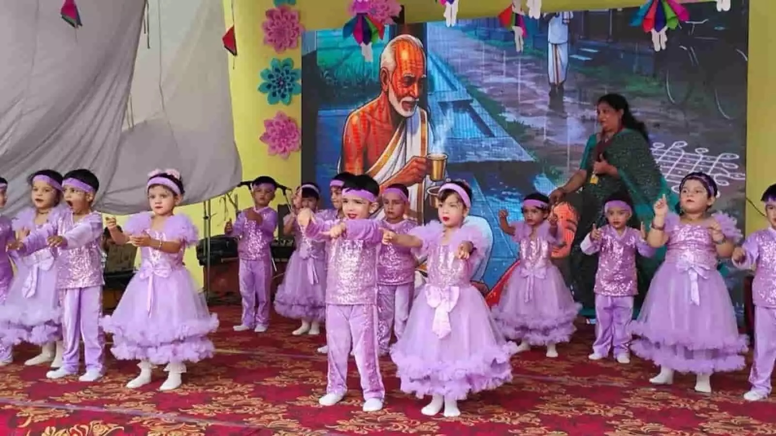बैंगनी पोशाक में बच्चे मंच पर नृत्य प्रस्तुत कर रहे हैं। बैंगनी पोशाक में बच्चे मंच पर नृत्य प्रस्तुत कर रहे हैं।
