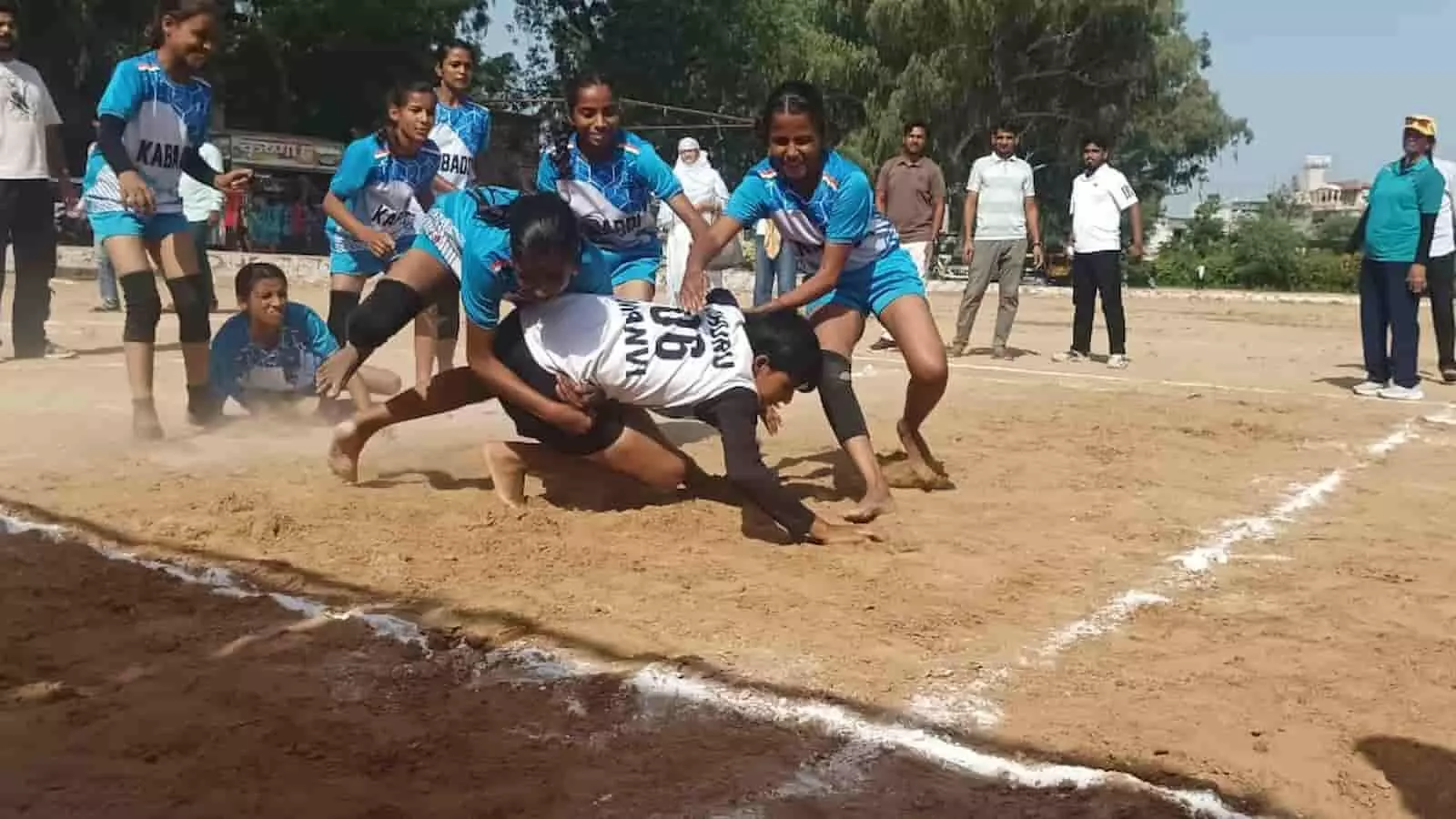 तस्वीर में मैदान पर नीली टी-शर्ट पहने खिलाड़ी विपक्षी टीम की रेडर को पकड़ते हुए दिख रहे हैं। तस्वीर में मैदान पर नीली टी-शर्ट पहने खिलाड़ी विपक्षी टीम की रेडर को पकड़ते हुए दिख रहे हैं।