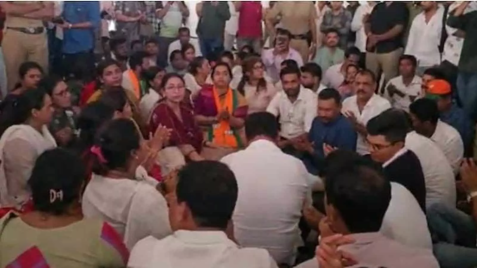 तस्वीर में दिख रही भीड़ जमीन पर बैठकर विरोध जता रही है और आसपास सुरक्षाकर्मी मौजूद हैं। तस्वीर में दिख रही भीड़ जमीन पर बैठकर विरोध जता रही है और आसपास सुरक्षाकर्मी मौजूद हैं।
