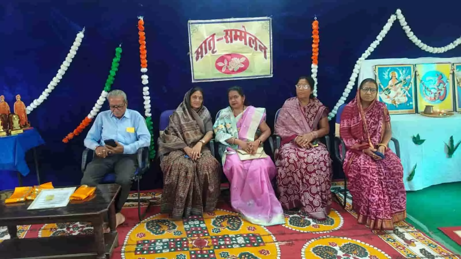 तस्वीर में बाएँ से दाएँ एक पुरुष और चार महिला अतिथि मातृ सम्मेलन के मंच पर बैठे हैं। तस्वीर में बाएँ से दाएँ एक पुरुष और चार महिला अतिथि मातृ सम्मेलन के मंच पर बैठे हैं।