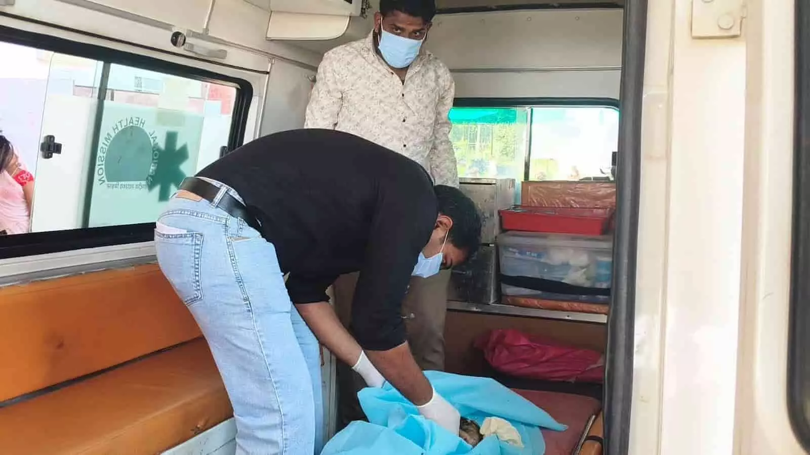 तस्वीर में एम्बुलेंस के भीतर बाईं ओर खड़े दो व्यक्ति नीले कपड़े में सामग्री संभाल रहे हैं। तस्वीर में एम्बुलेंस के भीतर बाईं ओर खड़े दो व्यक्ति नीले कपड़े में सामग्री संभाल रहे हैं।