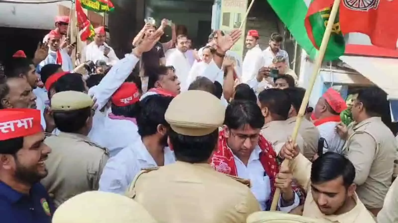 तस्वीर में सपा कार्यकर्ता लाल टोपी पहनकर पुलिसकर्मियों के बीच झंडा लहराकर विरोध प्रदर्शन कर रहे हैं। तस्वीर में सपा कार्यकर्ता लाल टोपी पहनकर पुलिसकर्मियों के बीच झंडा लहराकर विरोध प्रदर्शन कर रहे हैं।