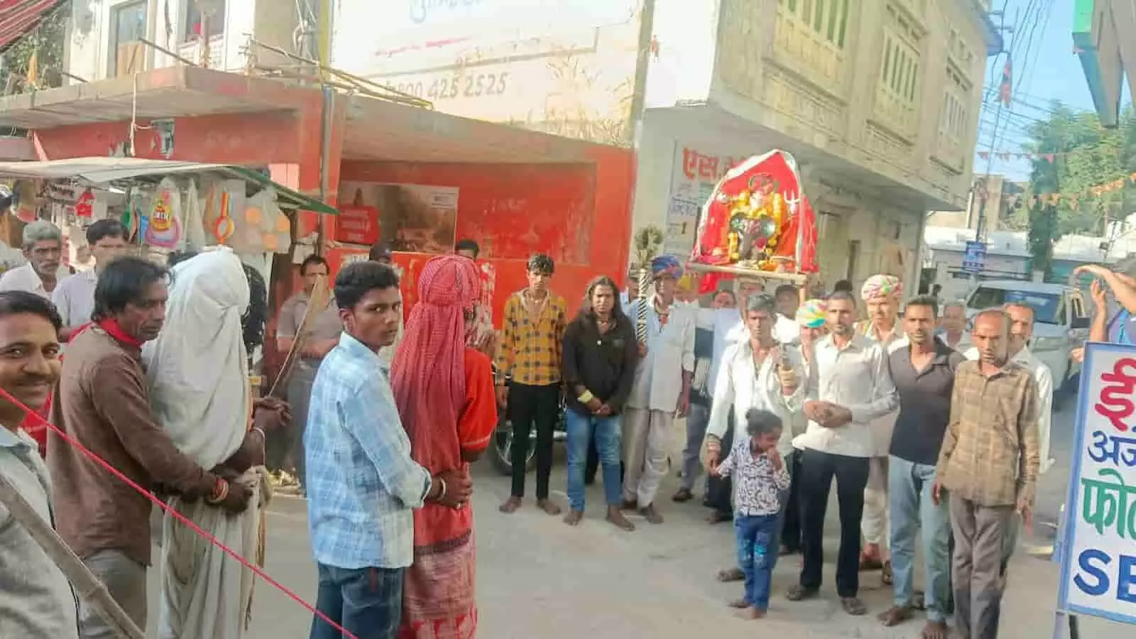 तस्वीर में गांव की सड़क पर खड़े ग्रामीण ढोल-नगाड़ों के साथ माता जी की सवारी लेकर जाते हुए दिख रहे हैं। तस्वीर में गांव की सड़क पर खड़े ग्रामीण ढोल-नगाड़ों के साथ माता जी की सवारी लेकर जाते हुए दिख रहे हैं।