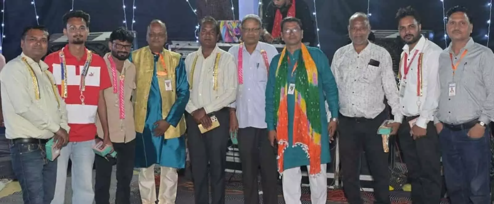 तस्वीर में बाएं से दाएं कई पुरुष गले में माला पहने एक साथ खड़े हैं। तस्वीर में बाएं से दाएं कई पुरुष गले में माला पहने एक साथ खड़े हैं।