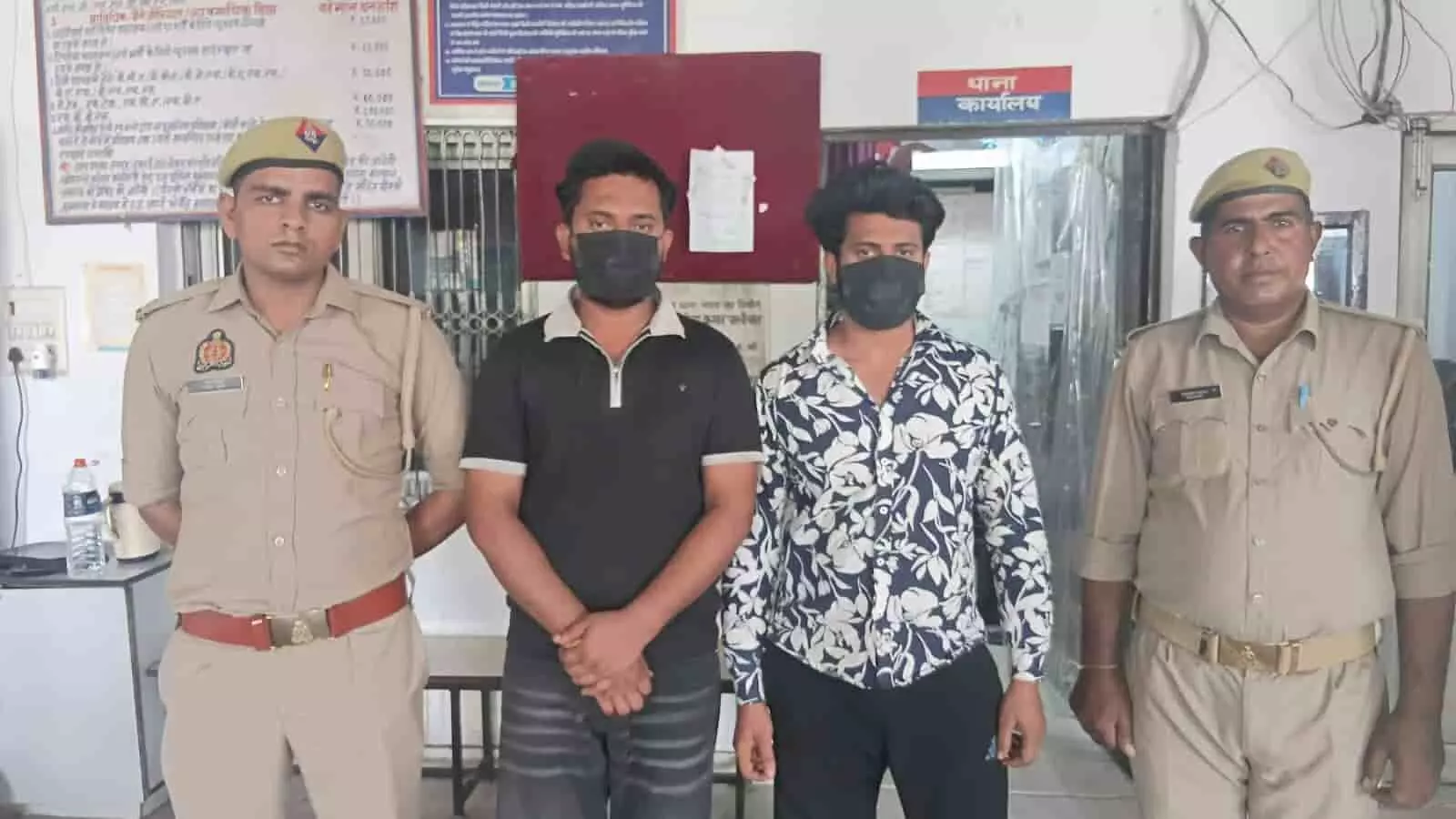 तस्वीर में बाएं से दाएं दो वर्दीधारी पुलिसकर्मी और उनके बीच मास्क पहने दो गिरफ्तार आरोपी खड़े हैं। तस्वीर में बाएं से दाएं दो वर्दीधारी पुलिसकर्मी और उनके बीच मास्क पहने दो गिरफ्तार आरोपी खड़े हैं।