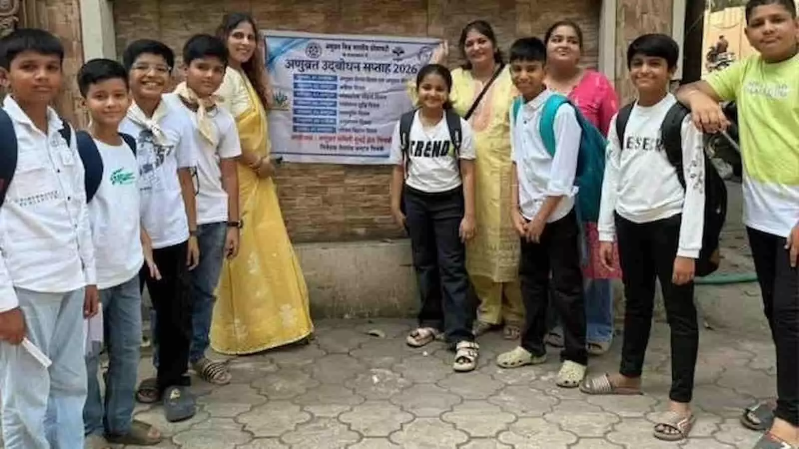 तस्वीर में दिख रही दीवार पर लगे पोस्टर के सामने बच्चे और महिलाएं साथ खड़े हैं। तस्वीर में दिख रही दीवार पर लगे पोस्टर के सामने बच्चे और महिलाएं साथ खड़े हैं।