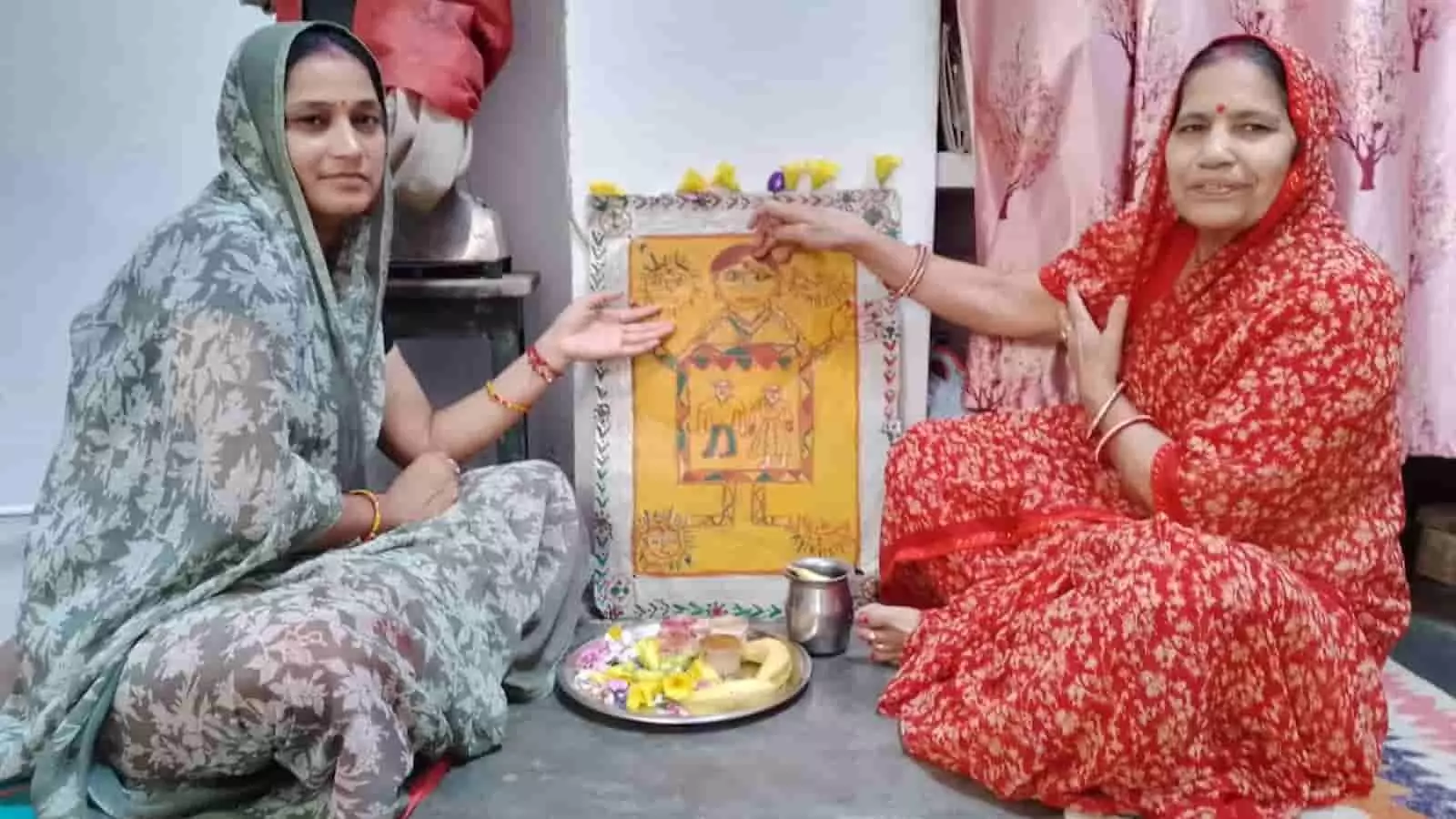 तस्वीर में बाईं ओर हरे रंग और दाईं ओर लाल रंग की साड़ी पहने महिलाएं सांझी कलाकृति की ओर हाथ कर रही हैं। तस्वीर में बाईं ओर हरे रंग और दाईं ओर लाल रंग की साड़ी पहने महिलाएं सांझी कलाकृति की ओर हाथ कर रही हैं।