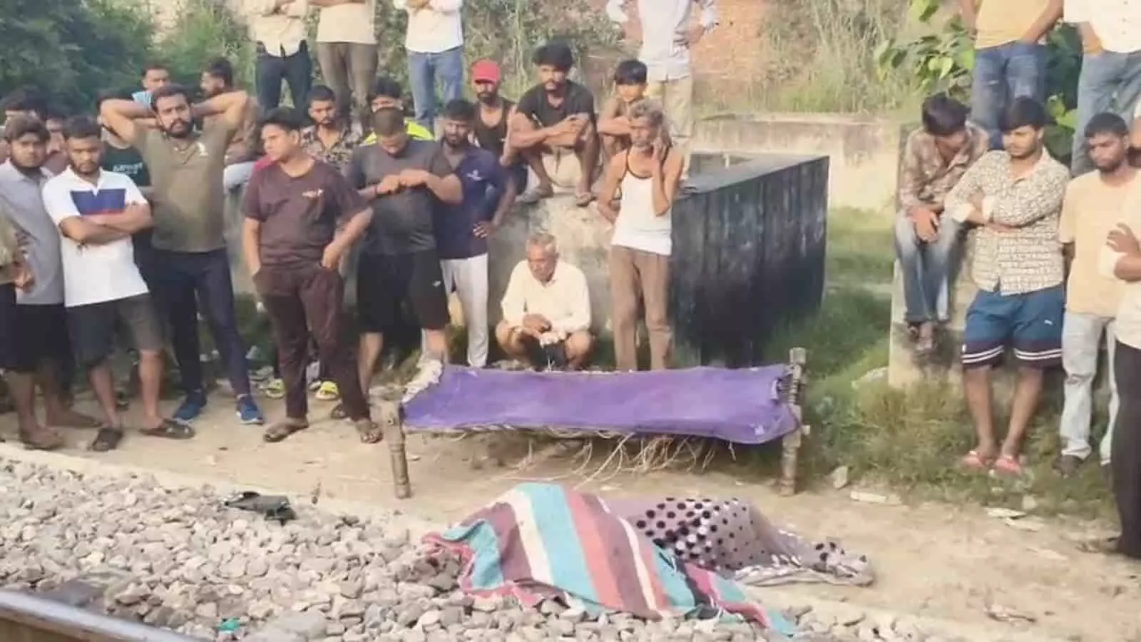 तस्वीर में रेलवे ट्रैक के किनारे कई लोग मौजूद हैं और जमीन पर ढका हुआ शव रखा है। तस्वीर में रेलवे ट्रैक के किनारे कई लोग मौजूद हैं और जमीन पर ढका हुआ शव रखा है।