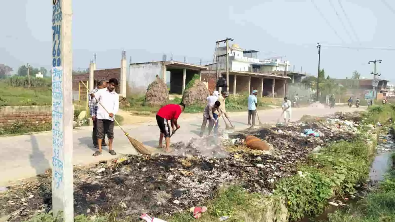 सड़क किनारे खड़े ग्रामीण और सफाईकर्मी हाथ में झाड़ू लेकर कचरा एकत्रित कर रहे हैं। सड़क किनारे खड़े ग्रामीण और सफाईकर्मी हाथ में झाड़ू लेकर कचरा एकत्रित कर रहे हैं।