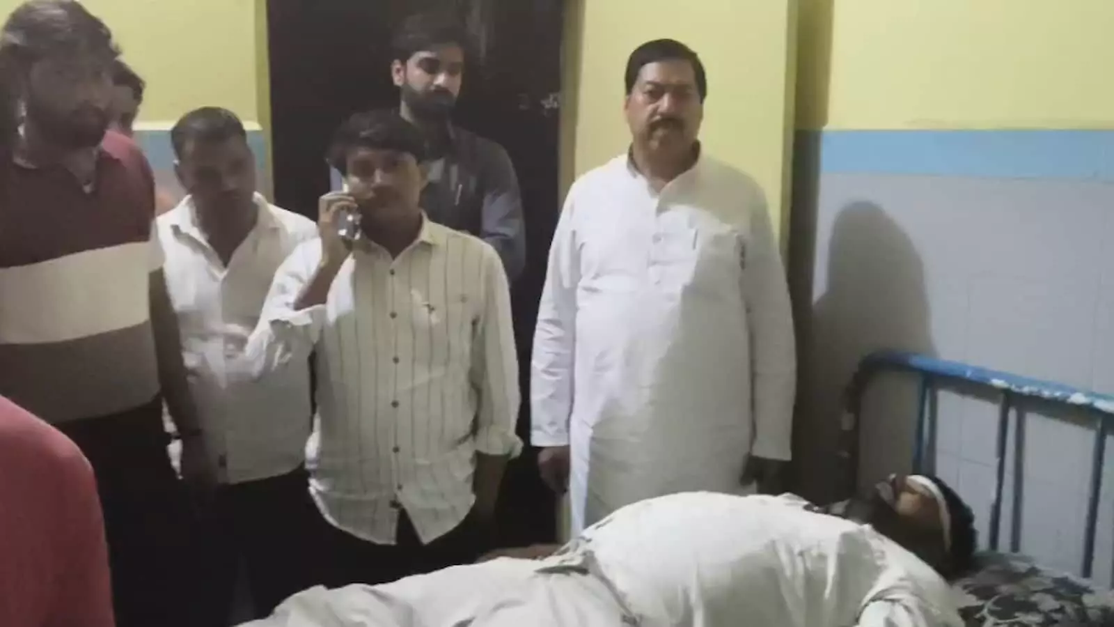 तस्वीर में अस्पताल के कमरे में सिर पर पट्टी बांधे लेटा मरीज और पास खड़े लोग नजर आ रहे हैं। तस्वीर में अस्पताल के कमरे में सिर पर पट्टी बांधे लेटा मरीज और पास खड़े लोग नजर आ रहे हैं।