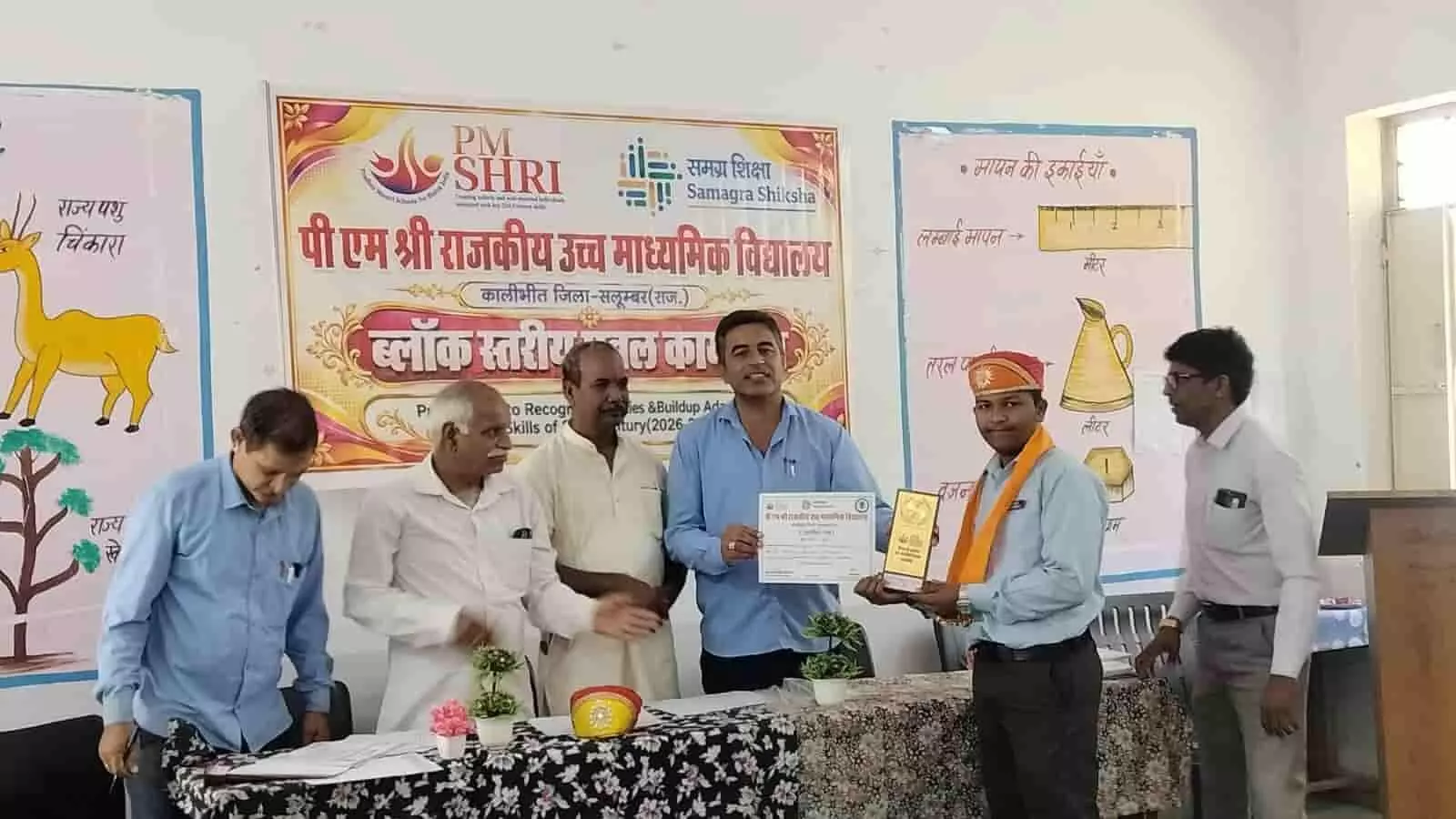 तस्वीर में बाएं से दाएं कई शिक्षक खड़े हैं और छात्र को ब्लॉक स्तरीय कार्यक्रम में सम्मानित कर रहे हैं। तस्वीर में बाएं से दाएं कई शिक्षक खड़े हैं और छात्र को ब्लॉक स्तरीय कार्यक्रम में सम्मानित कर रहे हैं।