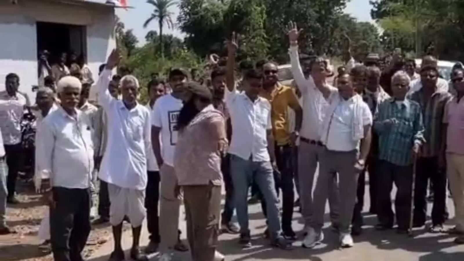 तस्वीर में एक मकान और सड़क के पास खड़े ग्रामीण हाथ उठाकर विरोध प्रदर्शन करते नजर आ रहे हैं। तस्वीर में एक मकान और सड़क के पास खड़े ग्रामीण हाथ उठाकर विरोध प्रदर्शन करते नजर आ रहे हैं।