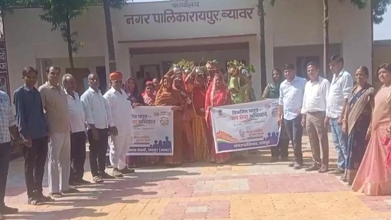 तस्वीर में नगर पालिका रायपुर ब्यावर परिसर में बैनर और सिर पर कलश रखे लोग खड़े हैं। तस्वीर में नगर पालिका रायपुर ब्यावर परिसर में बैनर और सिर पर कलश रखे लोग खड़े हैं।