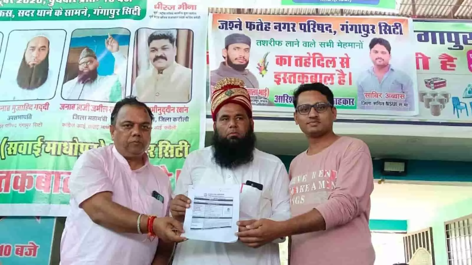 तस्वीर में बाएं से दाएं खड़े तीन लोग आपस में एक आवेदन पत्र सौंप रहे हैं। तस्वीर में बाएं से दाएं खड़े तीन लोग आपस में एक आवेदन पत्र सौंप रहे हैं।