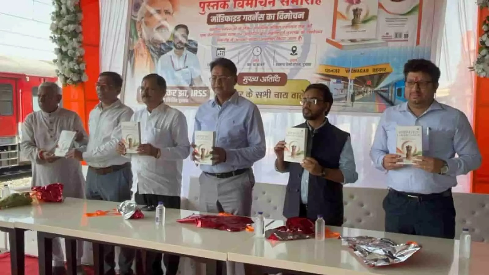तस्वीर में बाईं से दाईं ओर खड़े छह लोग एक मंच पर पुस्तक प्रदर्शित कर रहे हैं। तस्वीर में बाईं से दाईं ओर खड़े छह लोग एक मंच पर पुस्तक प्रदर्शित कर रहे हैं।