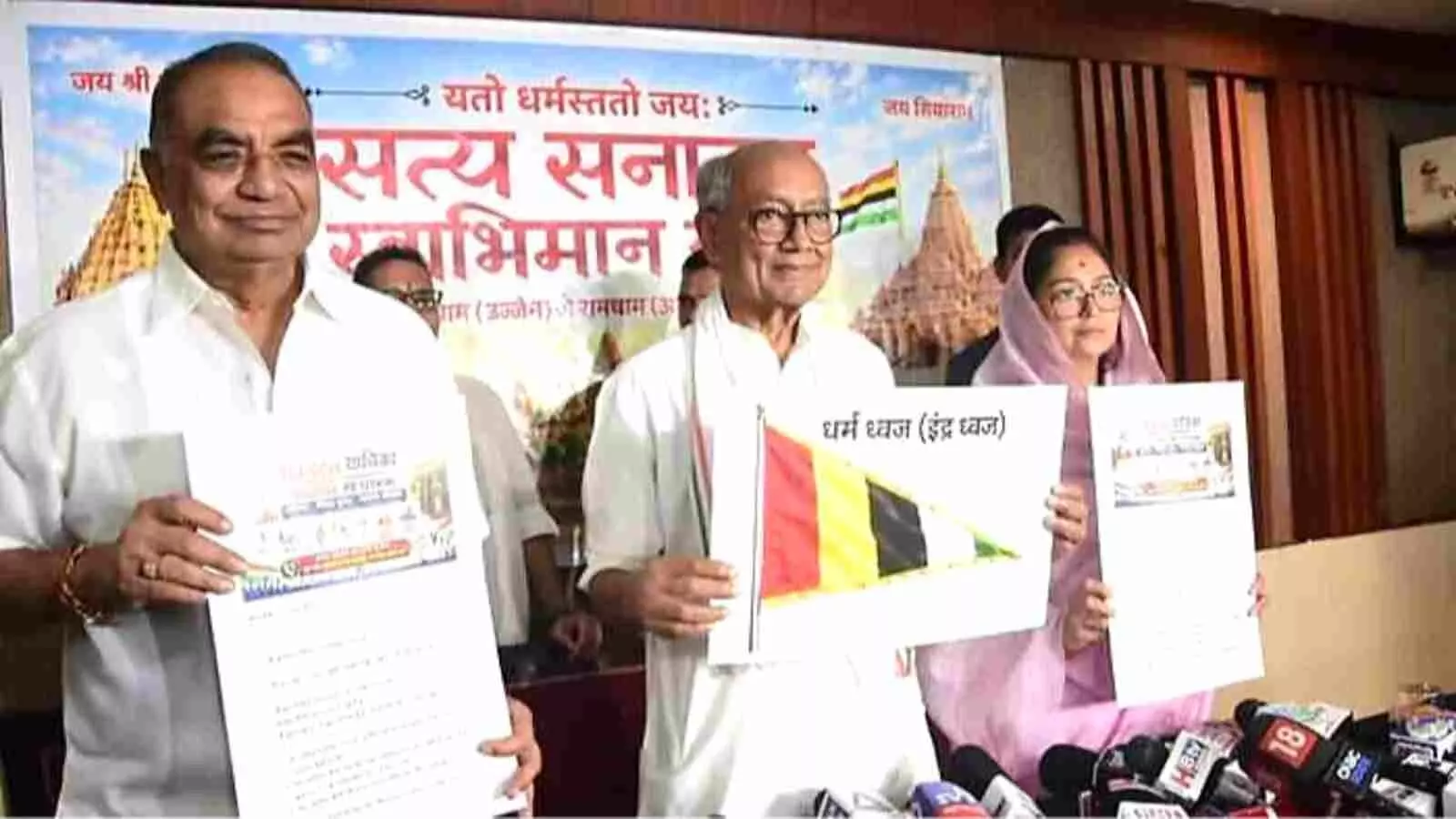 टेबल के पीछे खड़े होकर धर्मध्वज का चित्र और दस्तावेज हाथ में थामे दिग्विजय सिंह और उनकी पत्नी अमृता सिंह| टेबल के पीछे खड़े होकर धर्मध्वज का चित्र और दस्तावेज हाथ में थामे दिग्विजय सिंह और उनकी पत्नी अमृता सिंह|