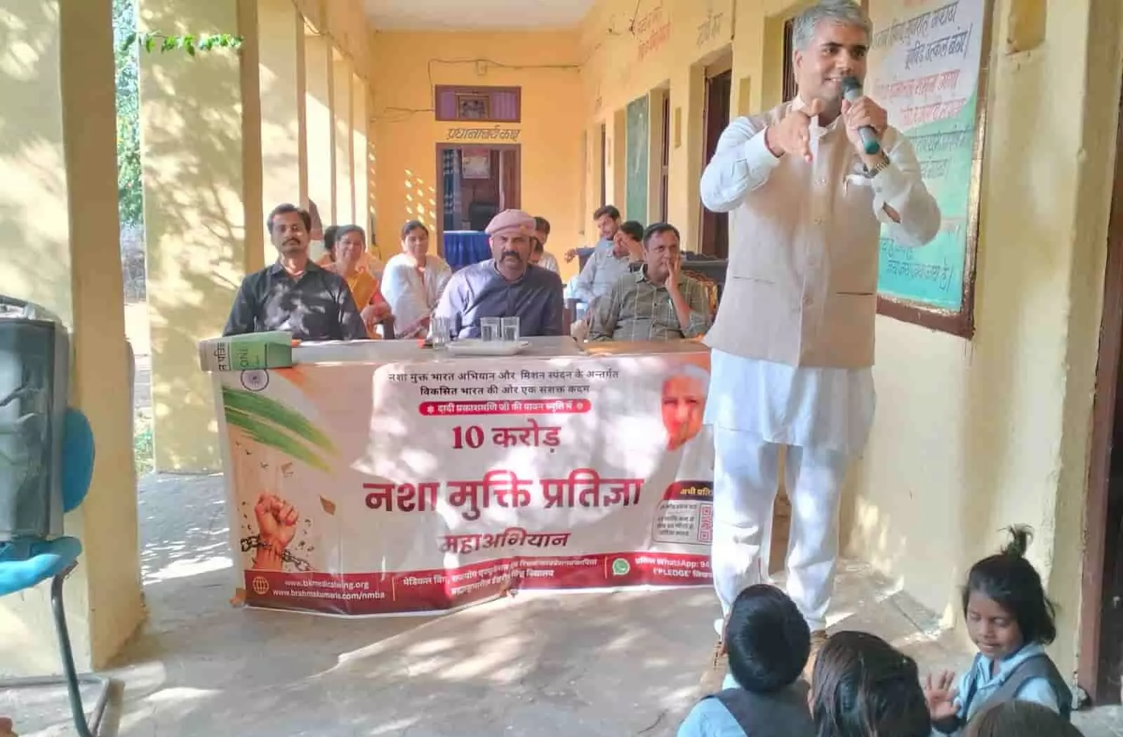 तस्वीर में दिख रही एक कुर्सी-मेज के पीछे अतिथि बैठे हैं और दाईं ओर खड़े सज्जन विद्यार्थियों को संबोधित कर रहे हैं। तस्वीर में दिख रही एक कुर्सी-मेज के पीछे अतिथि बैठे हैं और दाईं ओर खड़े सज्जन विद्यार्थियों को संबोधित कर रहे हैं।