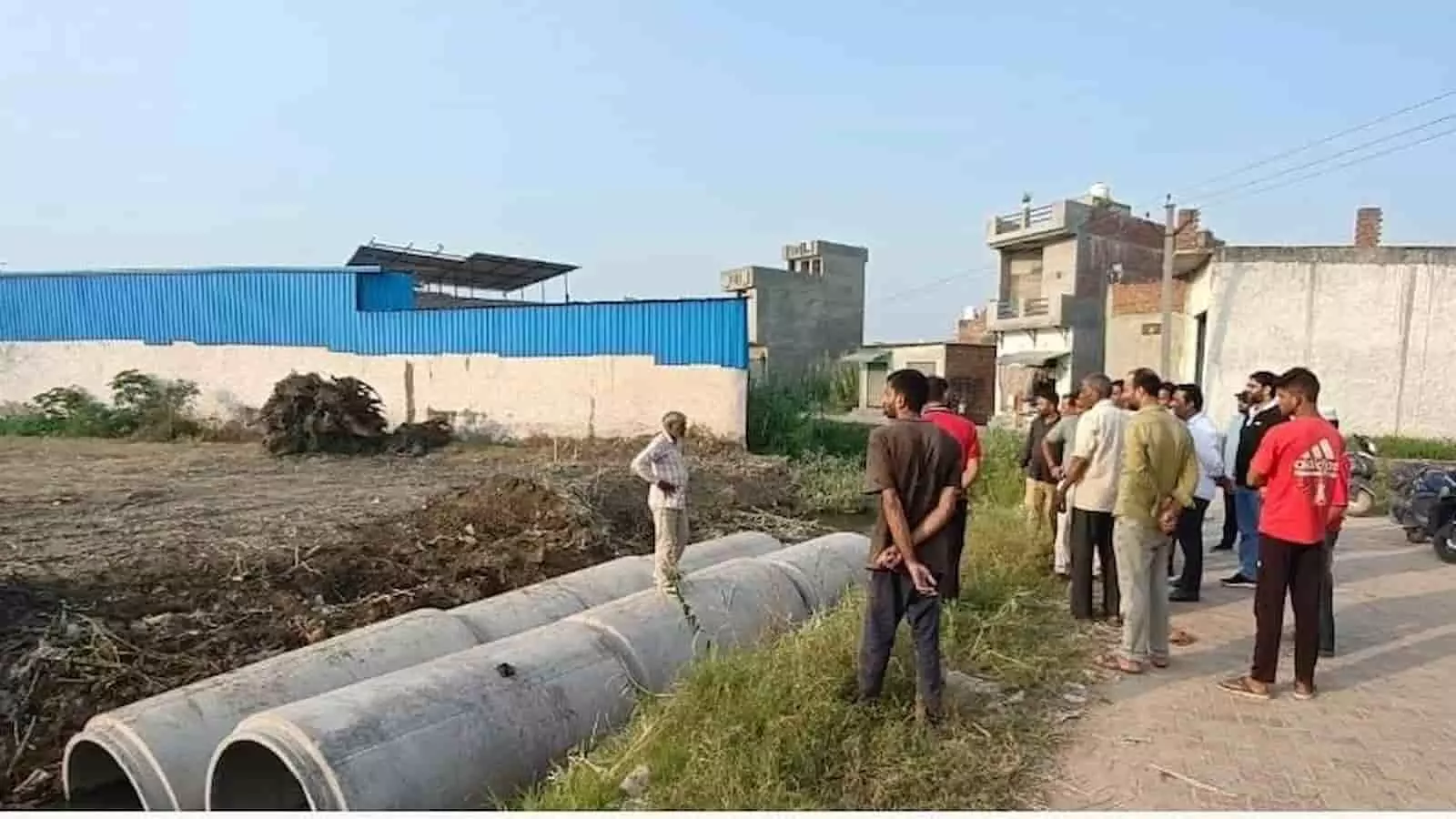 तस्वीर में दिख रही जगह पर कुछ लोग नाले के किनारे सीमेंट के पाइपों के पास खड़े हैं। तस्वीर में दिख रही जगह पर कुछ लोग नाले के किनारे सीमेंट के पाइपों के पास खड़े हैं।