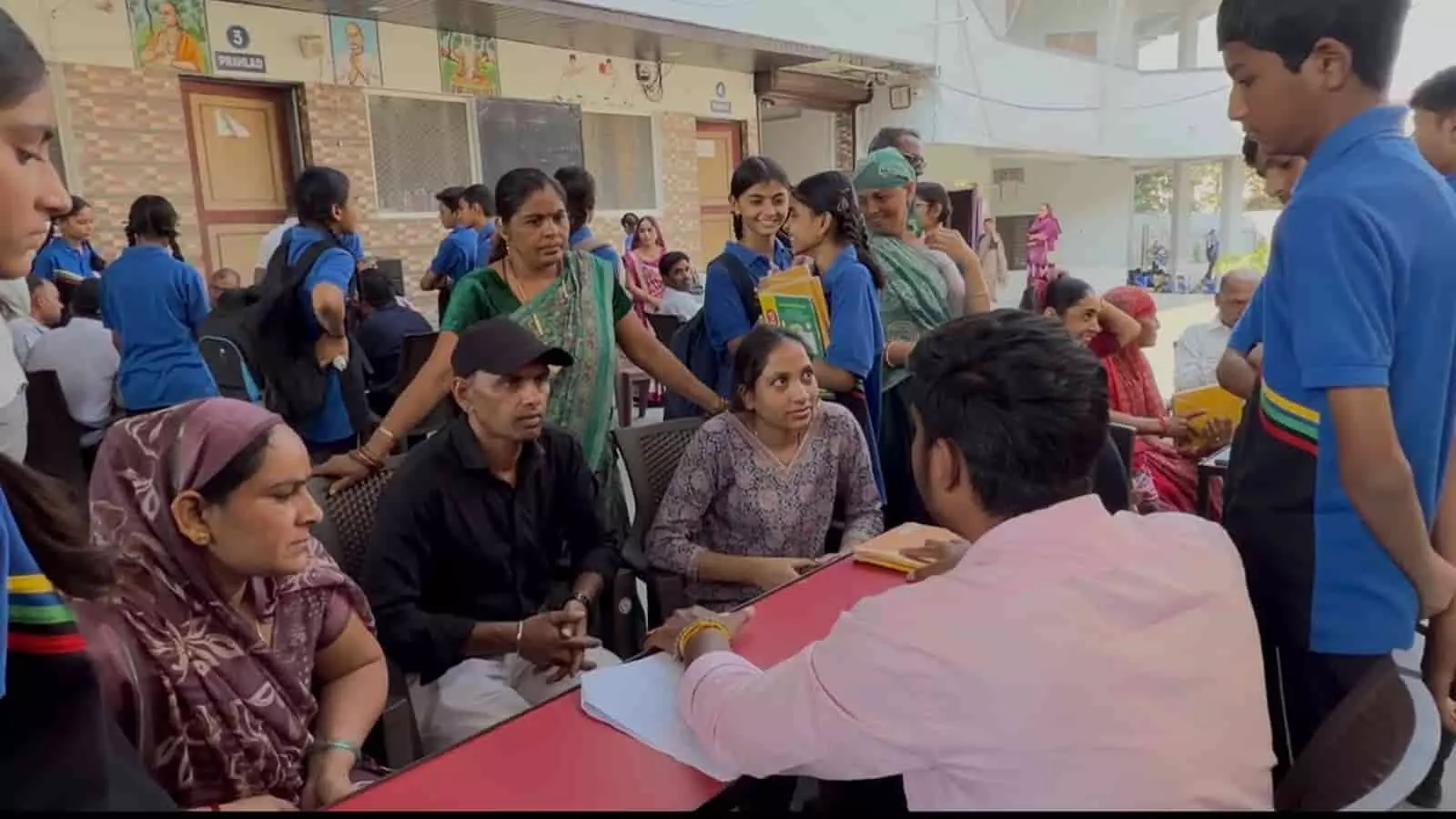 विद्यालय परिसर में शिक्षक से संवाद करते अभिभावक और नीली शर्ट में खड़े स्कूली छात्र। विद्यालय परिसर में शिक्षक से संवाद करते अभिभावक और नीली शर्ट में खड़े स्कूली छात्र।