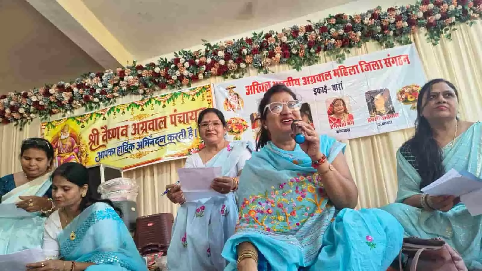 तस्वीर में मंच पर बैठी महिलाएं बैनर के सामने हाथ में कागज और माइक लिए कार्यक्रम आयोजित कर रही हैं। तस्वीर में मंच पर बैठी महिलाएं बैनर के सामने हाथ में कागज और माइक लिए कार्यक्रम आयोजित कर रही हैं।