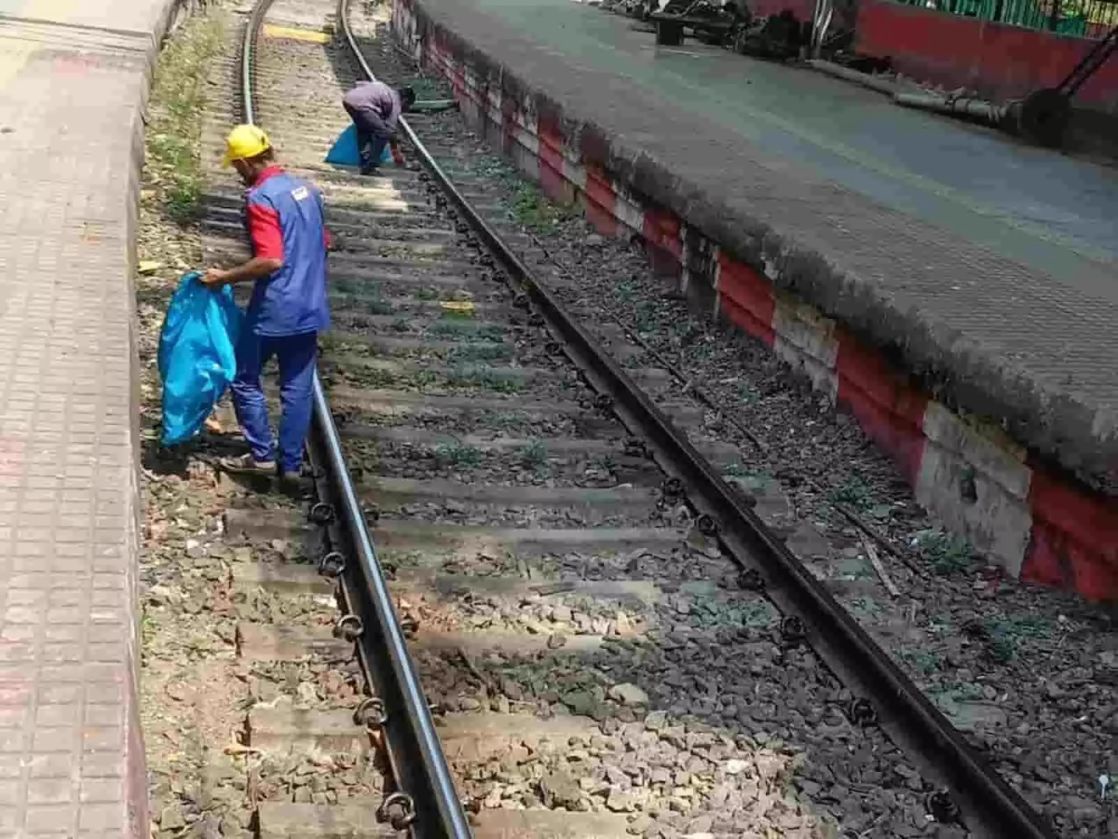 तस्वीर में दिख रही रेल पटरी पर खड़ा एक कर्मचारी बोरी में कचरा उठा रहा है और दूसरा आगे सफाई कर रहा है। तस्वीर में दिख रही रेल पटरी पर खड़ा एक कर्मचारी बोरी में कचरा उठा रहा है और दूसरा आगे सफाई कर रहा है।