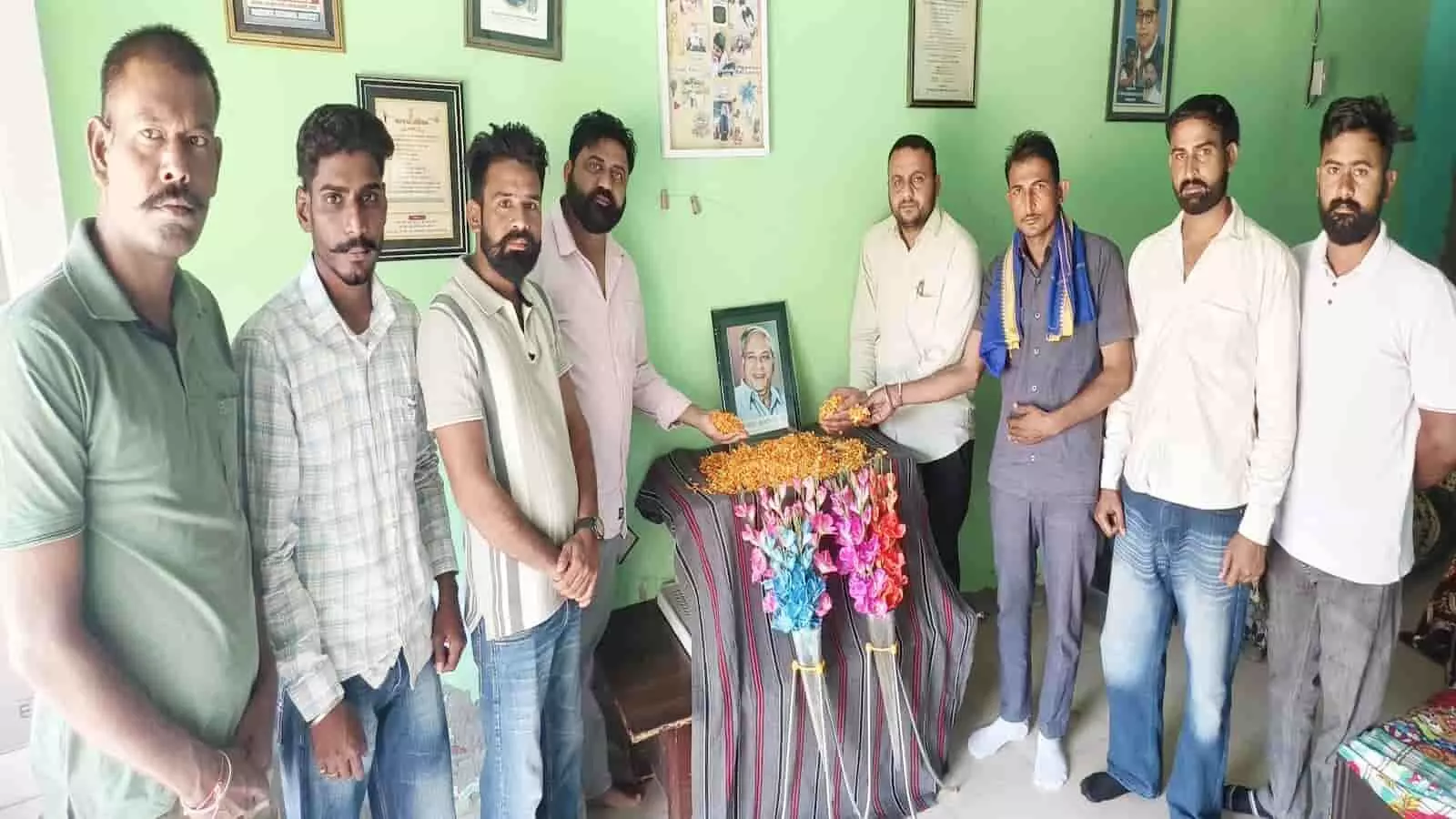 तस्वीर में बाएं से दाएं कई पुरुष कमरे में तस्वीर के पास खड़े दिख रहे हैं। तस्वीर में बाएं से दाएं कई पुरुष कमरे में तस्वीर के पास खड़े दिख रहे हैं।