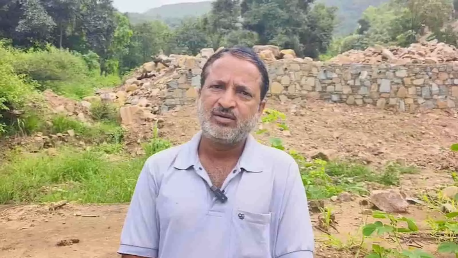 तस्वीर में पृष्ठभूमौ पाषाणभित्तिं निर्माणस्थलं च पृष्ठतः कृत्वा पुरतः तिष्ठन् विजय राम भीलः दृश्यते। तस्वीर में पृष्ठभूमौ पाषाणभित्तिं निर्माणस्थलं च पृष्ठतः कृत्वा पुरतः तिष्ठन् विजय राम भीलः दृश्यते।