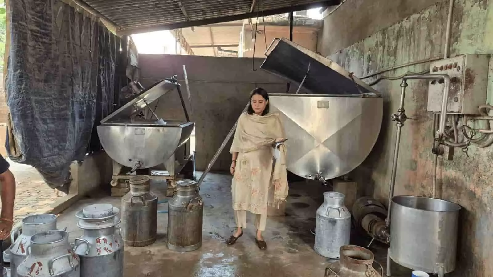 तस्वीर में बड़े बर्तनों और दूध के कनस्तरों के बीच खड़ी एक महिला अधिकारी दिखाई दे रही हैं। JPEG तस्वीर में बड़े बर्तनों और दूध के कनस्तरों के बीच खड़ी एक महिला अधिकारी दिखाई दे रही हैं। JPEG