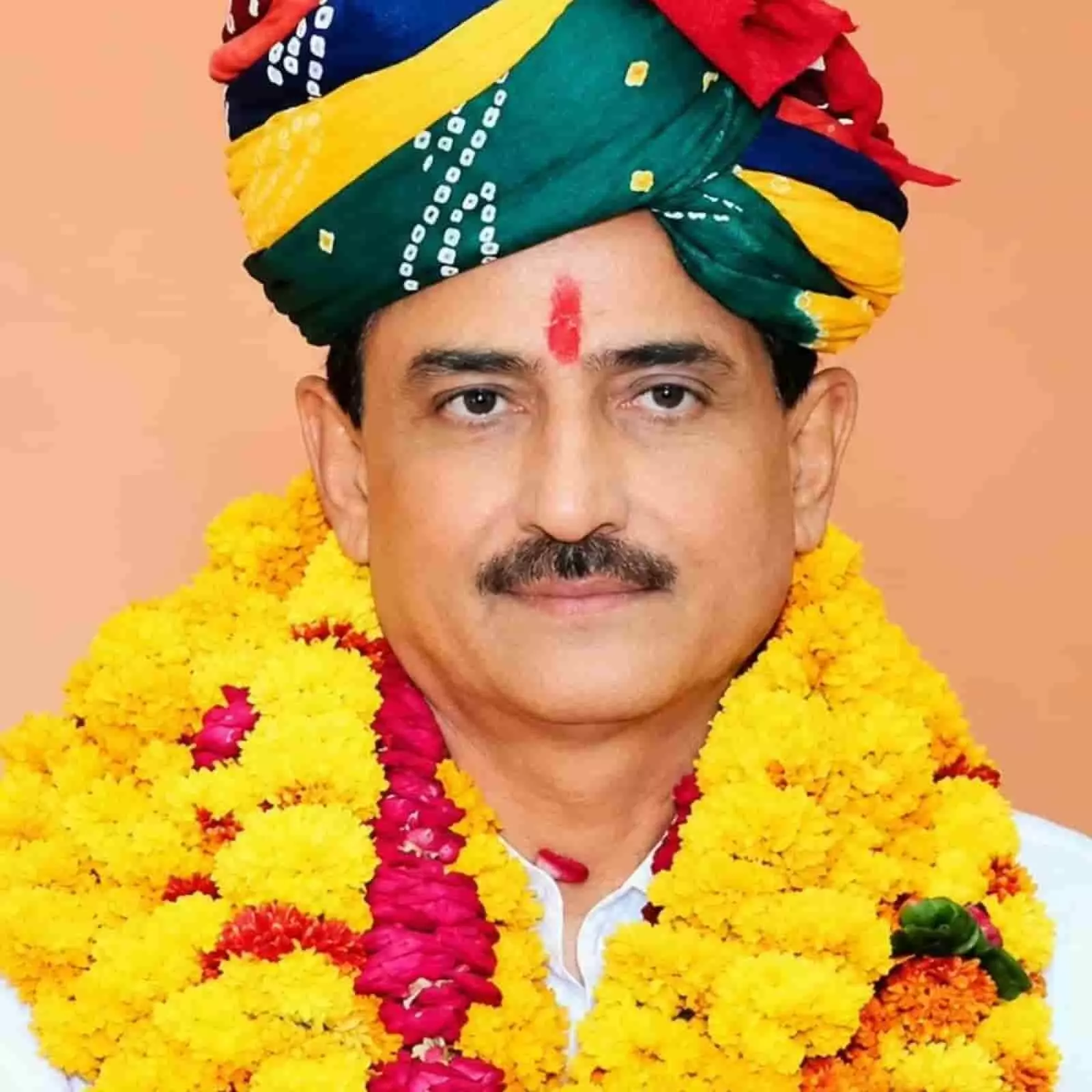 तस्वीर में रंग-बिरंगी पगड़ी और गेंदे के फूलों की माला पहने एक व्यक्ति सामने देख रहा है। तस्वीर में रंग-बिरंगी पगड़ी और गेंदे के फूलों की माला पहने एक व्यक्ति सामने देख रहा है।