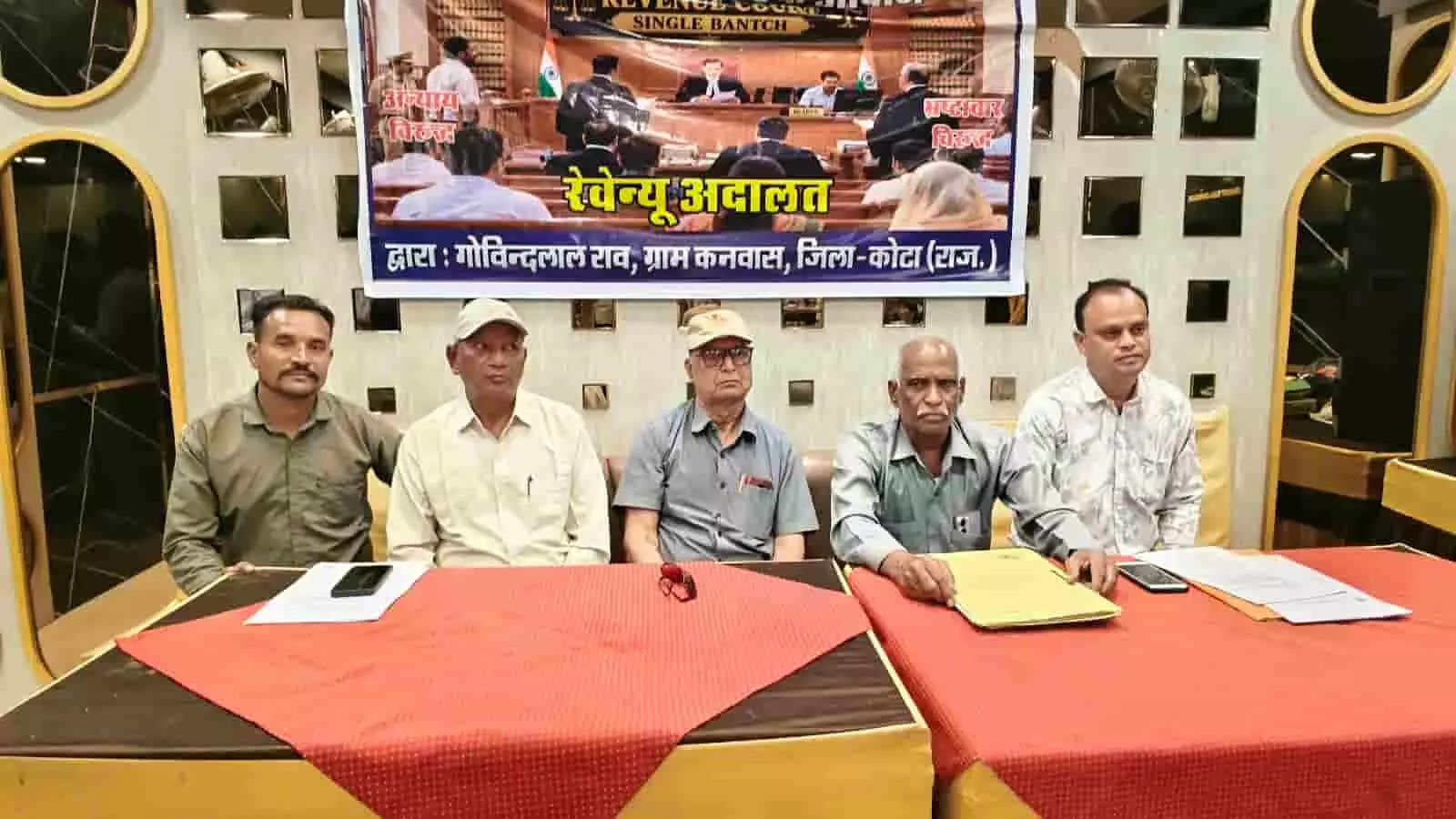 एक मेज के पीछे बैठे बुजुर्ग गोविंद लाल और उनके साथी प्रेस वार्ता कर रहे हैं। एक मेज के पीछे बैठे बुजुर्ग गोविंद लाल और उनके साथी प्रेस वार्ता कर रहे हैं।