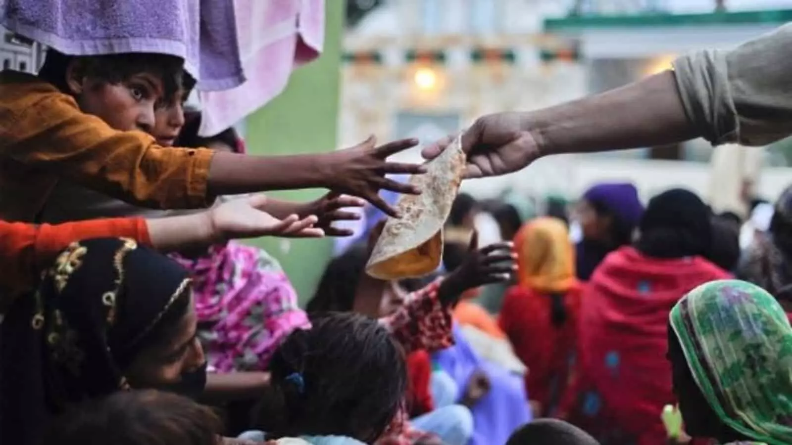 तस्वीर में भोजन वितरण के दौरान एक व्यक्ति से रोटी लेने के लिए हाथ बढ़ाते बच्चे दिख रहे हैं। तस्वीर में भोजन वितरण के दौरान एक व्यक्ति से रोटी लेने के लिए हाथ बढ़ाते बच्चे दिख रहे हैं।