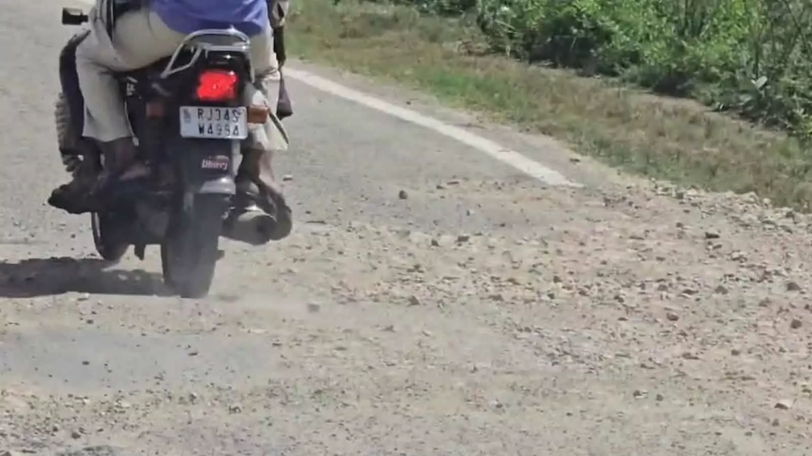 तस्वीर में क्षतिग्रस्त और कंक्रीट उखड़ी सड़क से गुजरता हुआ एक मोटरसाइकिल चालक। तस्वीर में क्षतिग्रस्त और कंक्रीट उखड़ी सड़क से गुजरता हुआ एक मोटरसाइकिल चालक।