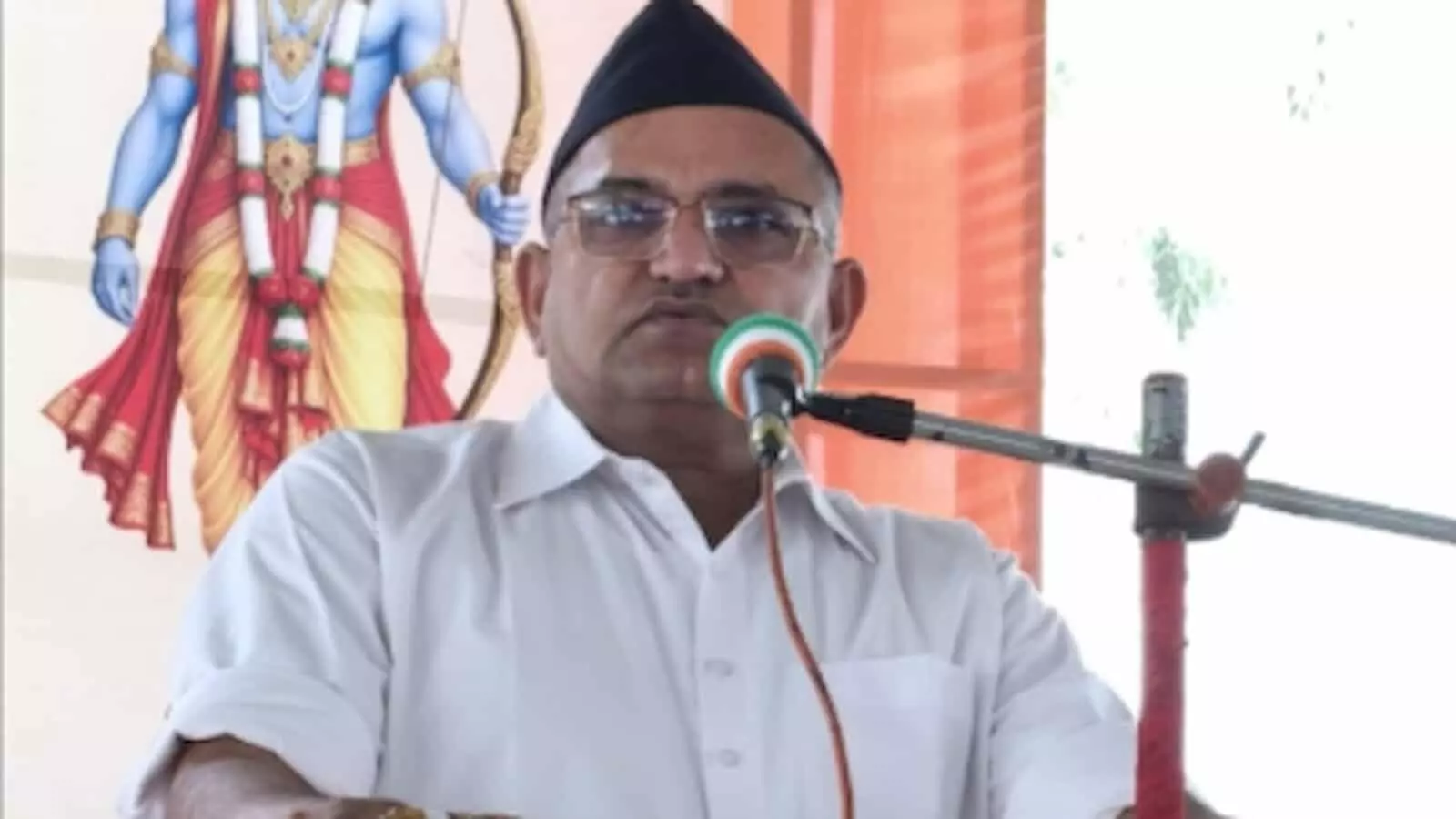 तस्वीर में एक व्यक्ति मंच पर माइक के सामने खड़े होकर भाषण देते हुए दिख रहे हैं। तस्वीर में एक व्यक्ति मंच पर माइक के सामने खड़े होकर भाषण देते हुए दिख रहे हैं।