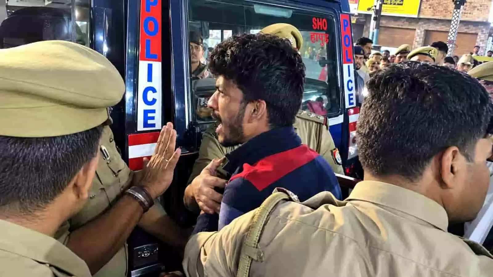 तस्वीर में हापुड़ में पुलिस गाड़ी के पास पुलिसकर्मी एक युवक को पकड़ते दिख रहे हैं। तस्वीर में हापुड़ में पुलिस गाड़ी के पास पुलिसकर्मी एक युवक को पकड़ते दिख रहे हैं।