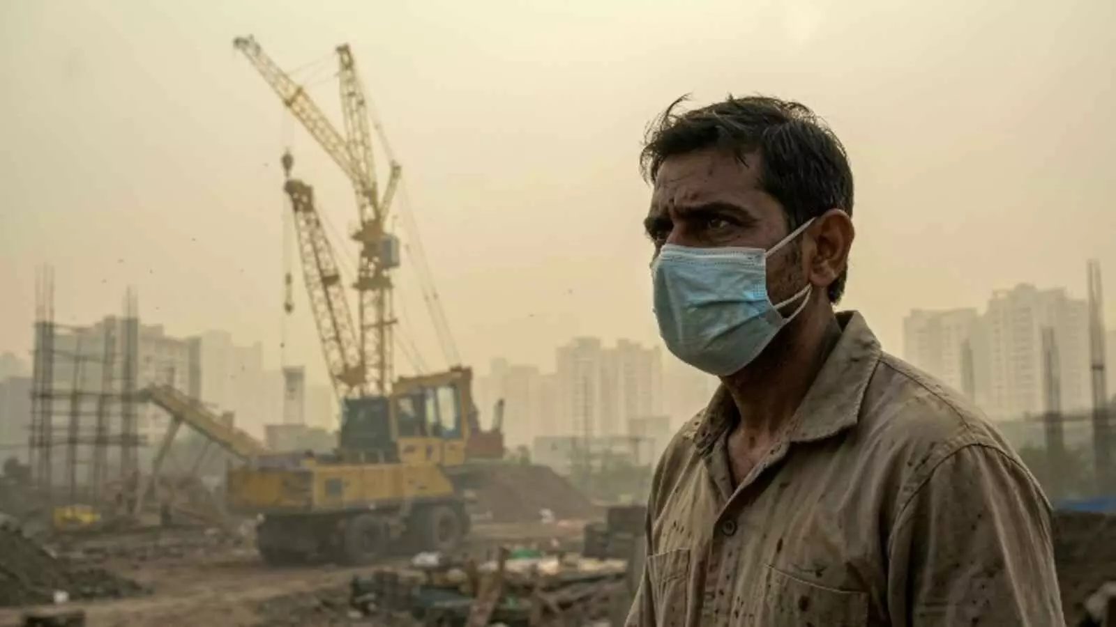 धुंध के बीच मास्क पहने व्यक्ति और क्रेन नोएडा में निर्माण स्थल के संदर्भ में दिख रहे हैं। धुंध के बीच मास्क पहने व्यक्ति और क्रेन नोएडा में निर्माण स्थल के संदर्भ में दिख रहे हैं।