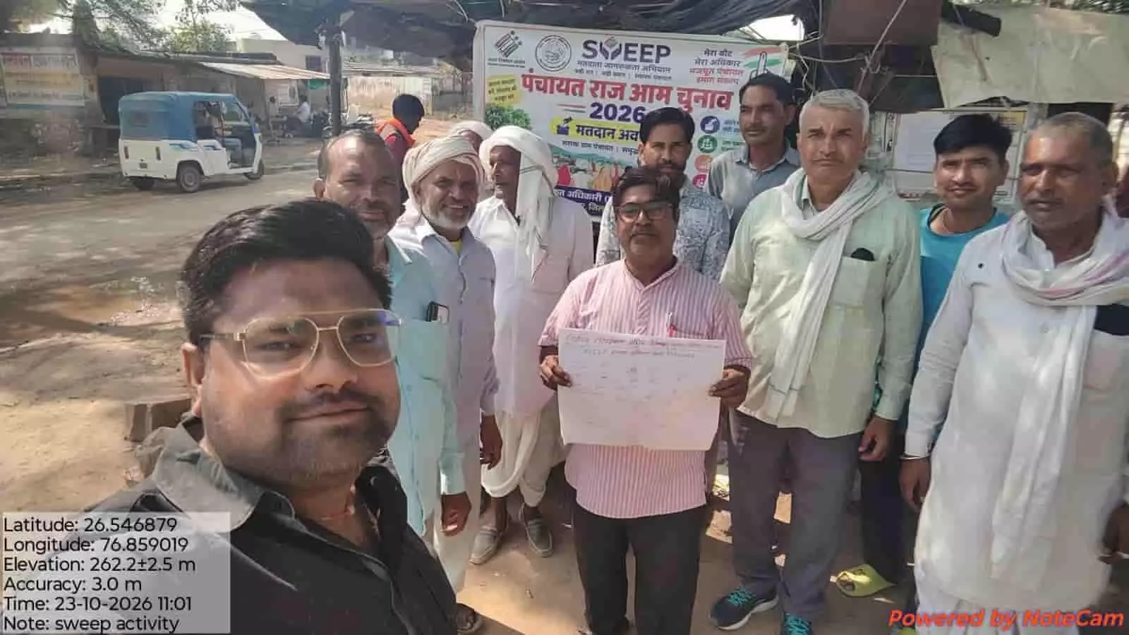 तस्वीर में स्वीप बैनर के सामने ग्रामीण और अधिकारी मतदाता जागरूकता अभियान के दौरान खड़े दिख रहे हैं। तस्वीर में स्वीप बैनर के सामने ग्रामीण और अधिकारी मतदाता जागरूकता अभियान के दौरान खड़े दिख रहे हैं।