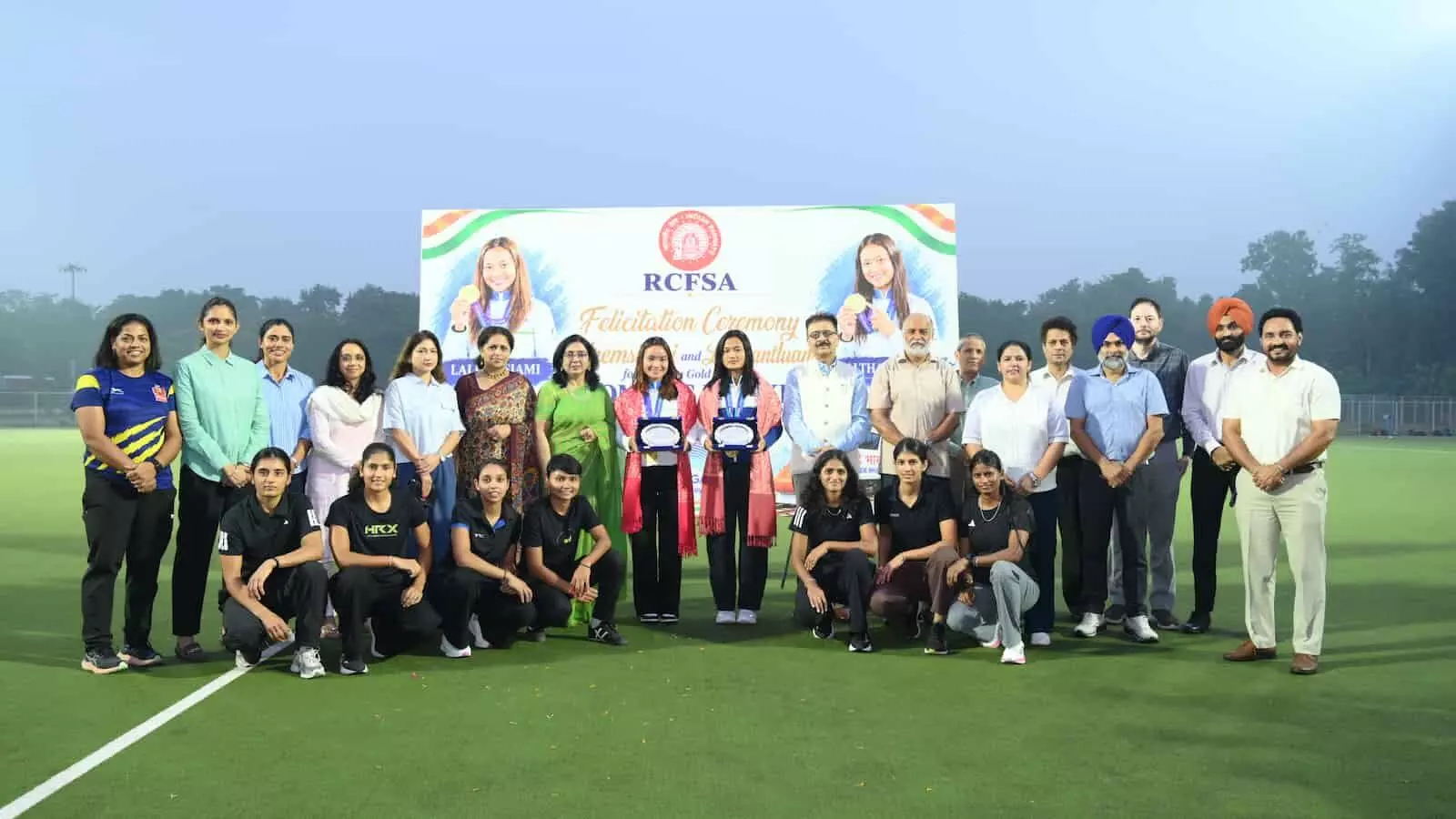 तस्वीर में हॉकी खिलाड़ी लालरेम्सियामी और ललथांतलुआंगी आरसीएफ कपूरथला के एस्ट्रोटर्फ मैदान में अधिकारियों के साथ खड़ी हैं।