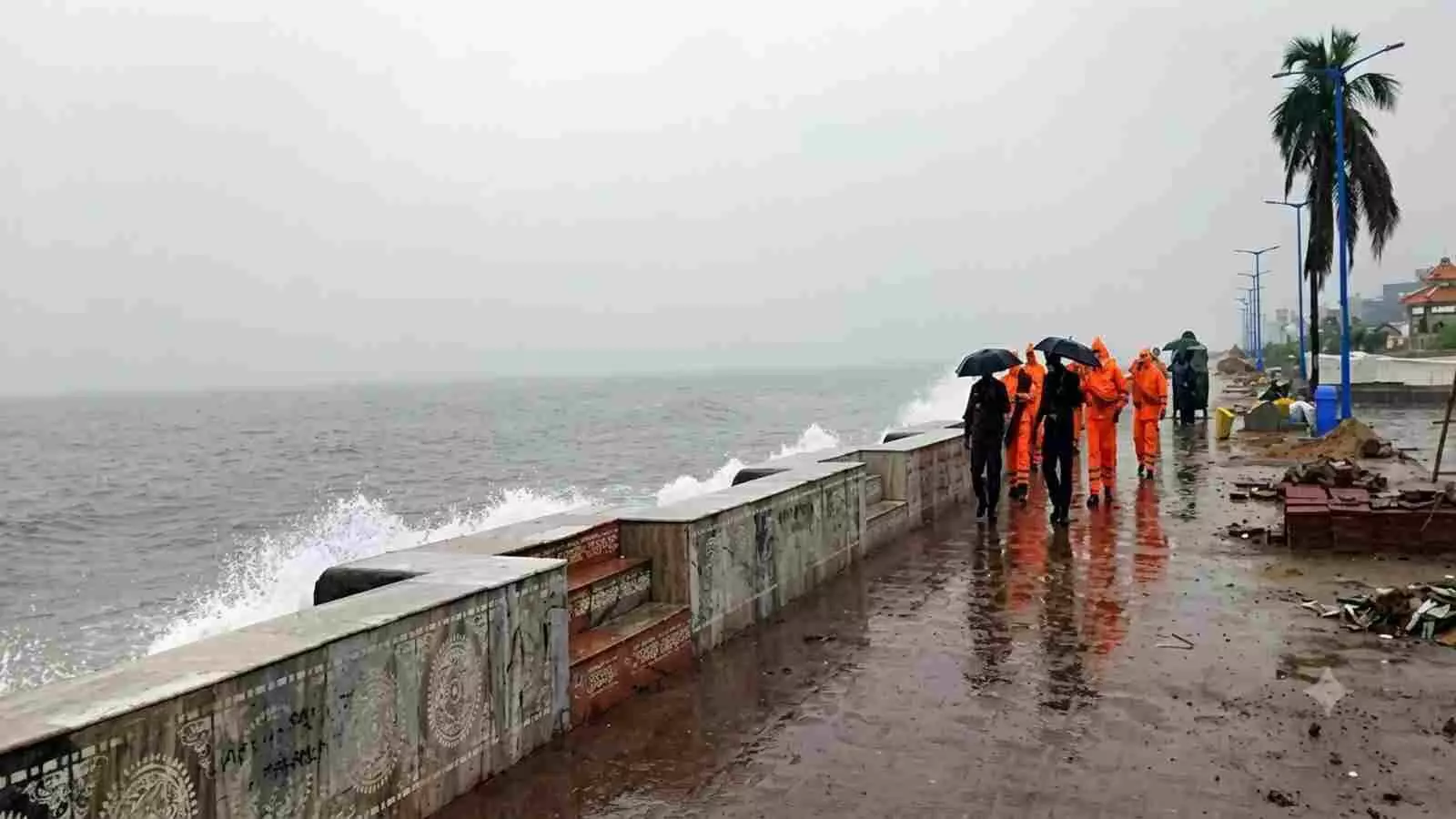 बारिश और तेज हवाओं के बीच समुद्र तट पर चलते लोग और सुरक्षाकर्मी|
