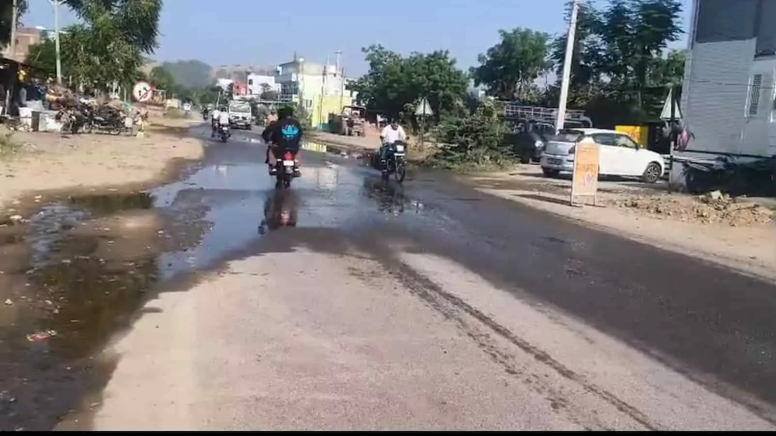 तस्वीर में खेरवाड़ा के NH-927A पर बीएसएनएल कार्यालय के सामने सड़क पर जमा गंदे पानी से गुजरते दोपहिया वाहन चालक दिख रहे हैं।