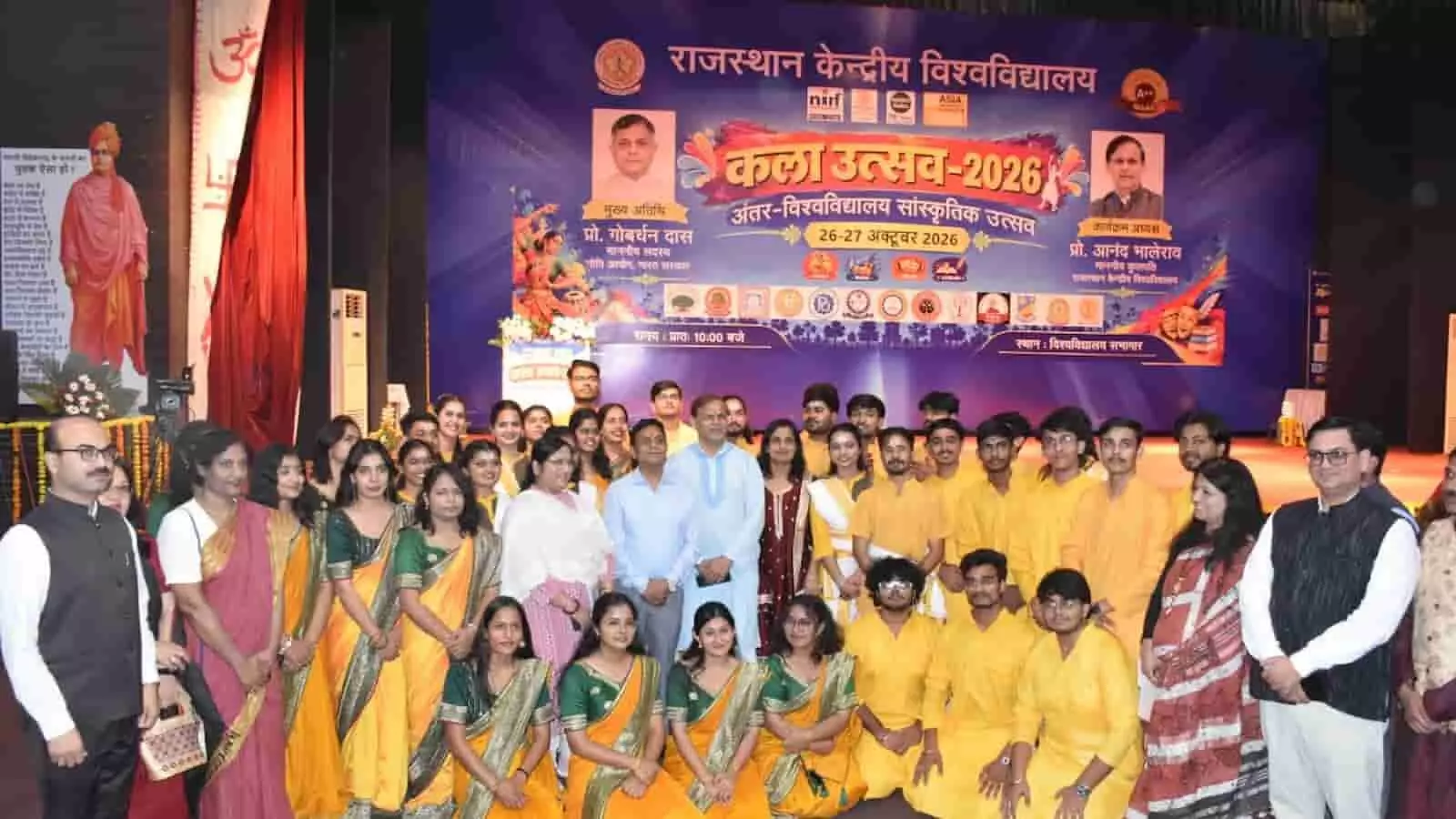 तस्वीर में राजस्थान केंद्रीय विश्वविद्यालय के सभागार में कला-उत्सव 2026 के उद्घाटन समारोह के दौरान मंचासीन अतिथियों संग प्रतिभागी खड़े हैं।