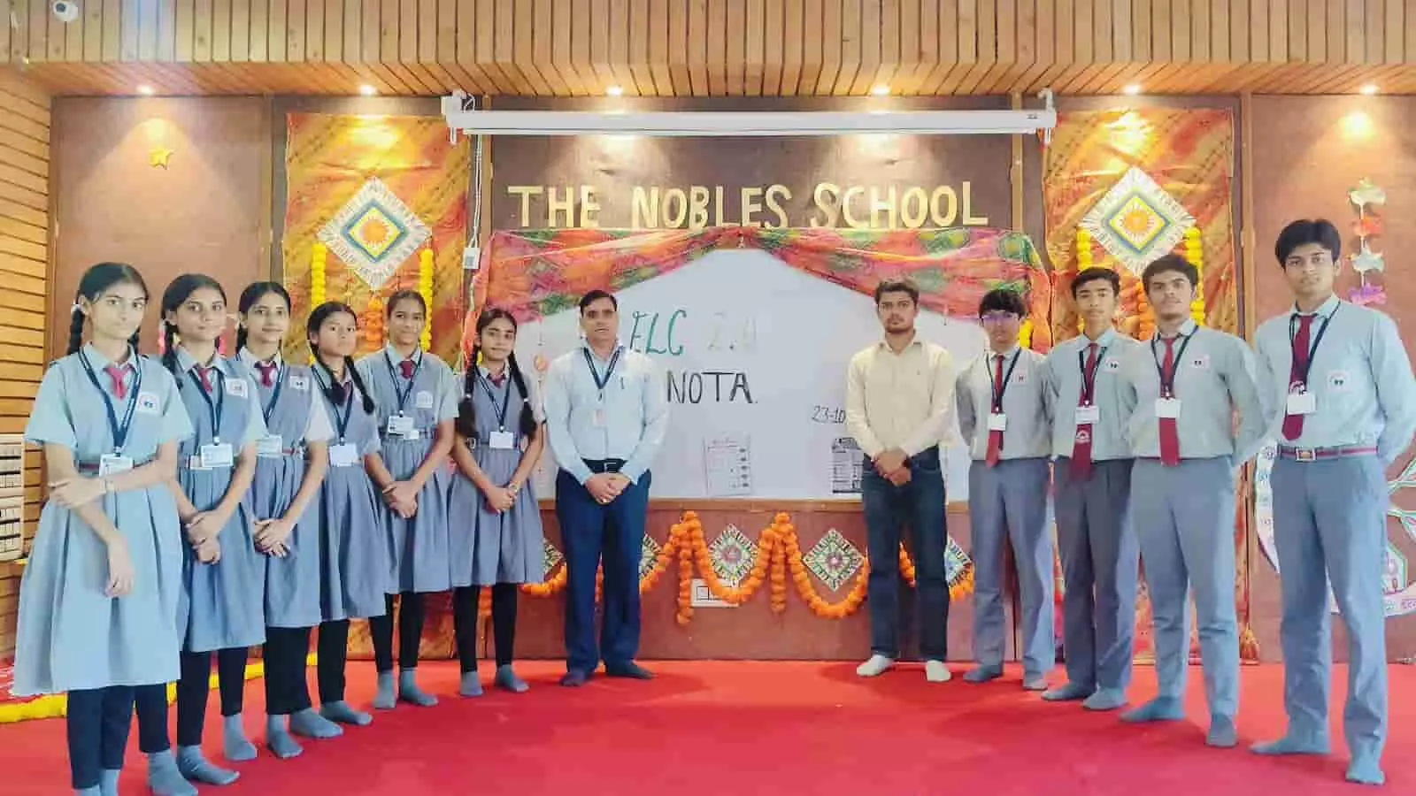 तस्वीर में द नोबल्स स्कूल के कार्यक्रम में छात्र और शिक्षक खड़े दिखाई दे रहे हैं। तस्वीर में द नोबल्स स्कूल के कार्यक्रम में छात्र और शिक्षक खड़े दिखाई दे रहे हैं।