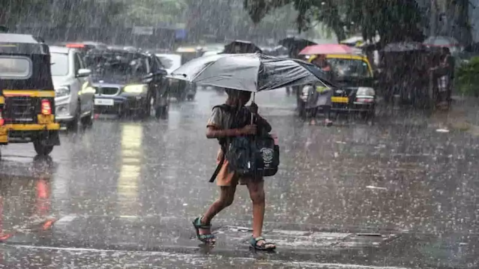 तस्वीर में... बारिश के बीच छाता लिए सड़क पार करता एक स्कूली बच्चा नजर आ रहा है।