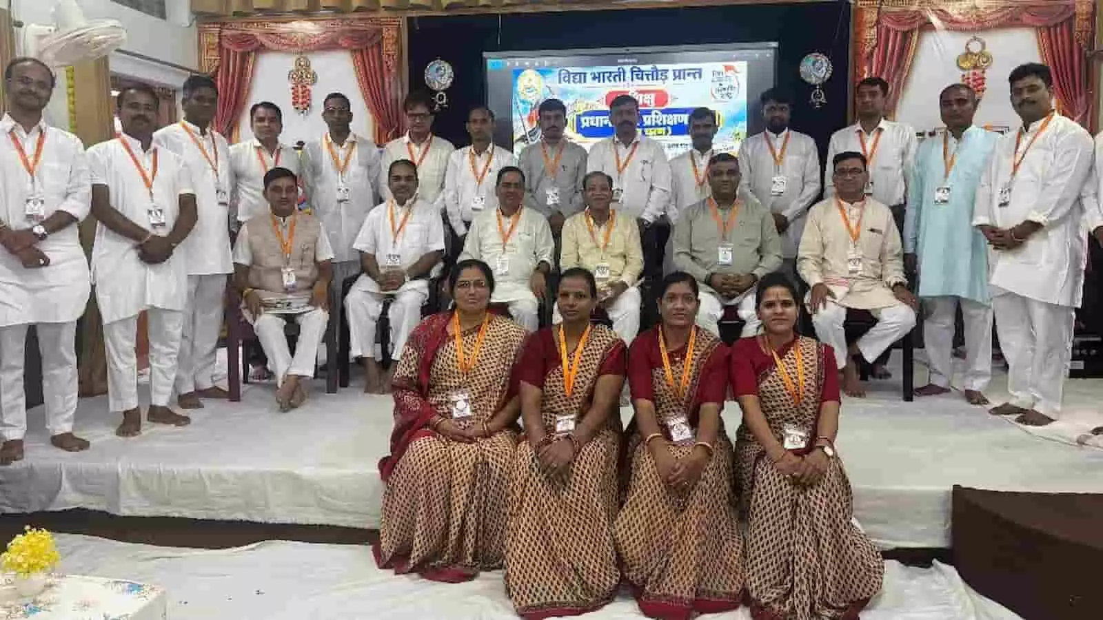 तस्वीर में चित्तौड़गढ़ के प्रशिक्षण केंद्र में विद्या भारती कार्यक्रम के दौरान मंच पर समूह में बैठे और खड़े प्रतिभागी दिख रहे हैं। तस्वीर में चित्तौड़गढ़ के प्रशिक्षण केंद्र में विद्या भारती कार्यक्रम के दौरान मंच पर समूह में बैठे और खड़े प्रतिभागी दिख रहे हैं।
